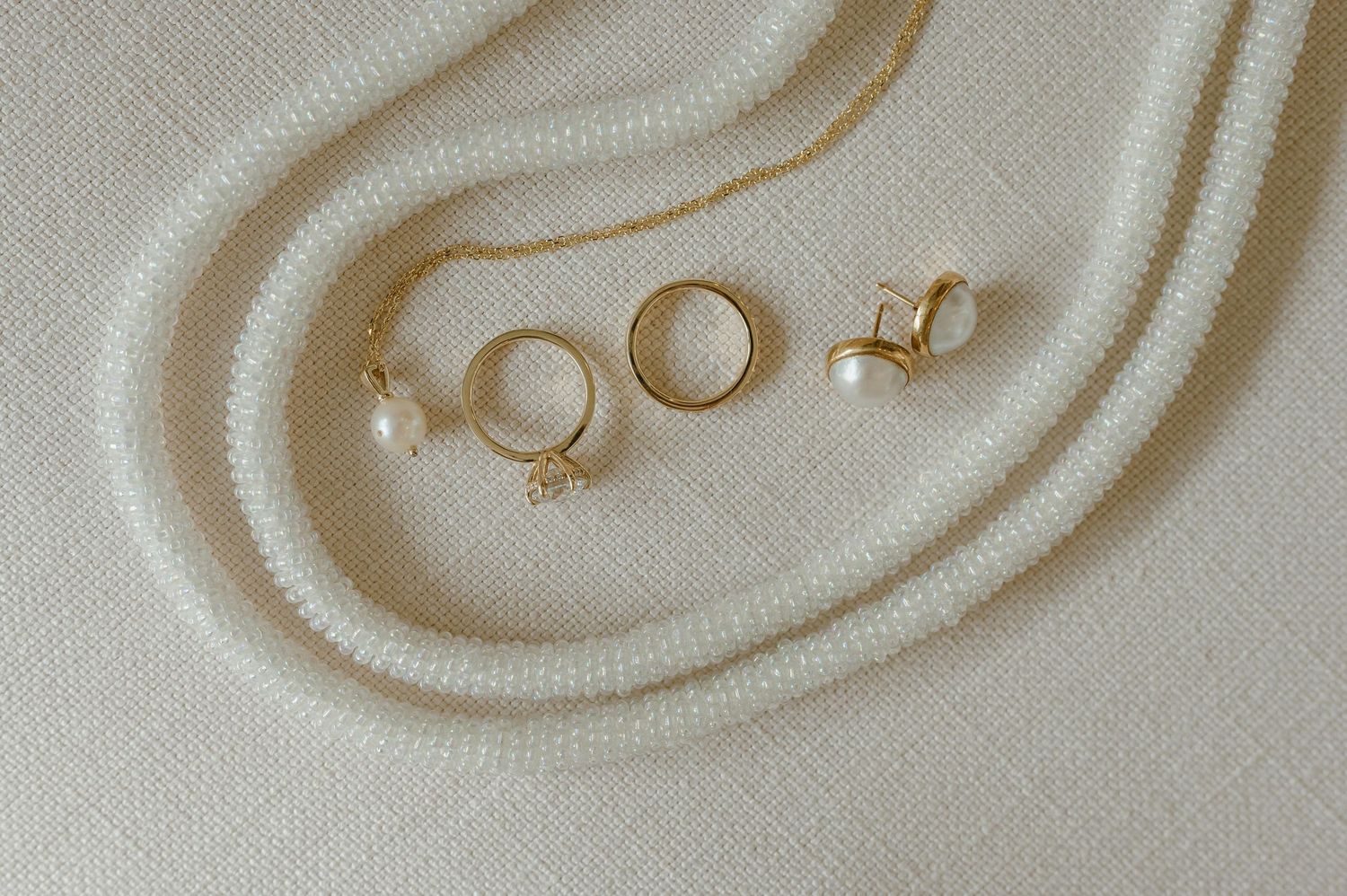 Gold wedding rings and earrings arranged on a soft white fabric with delicate folds creating an elegant composition.