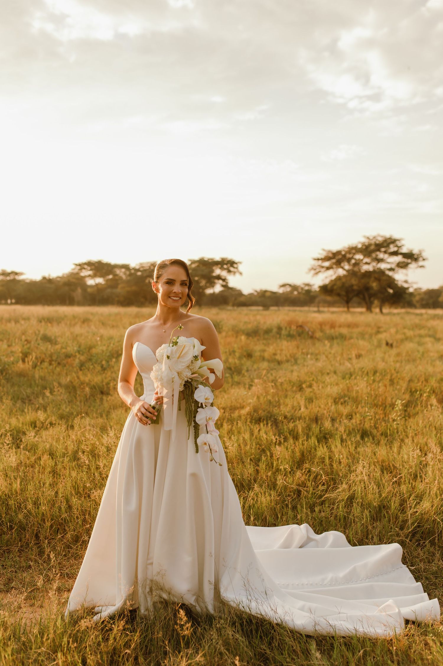 A flowing white wedding dress trails beautifully across a sunlit savanna landscape.