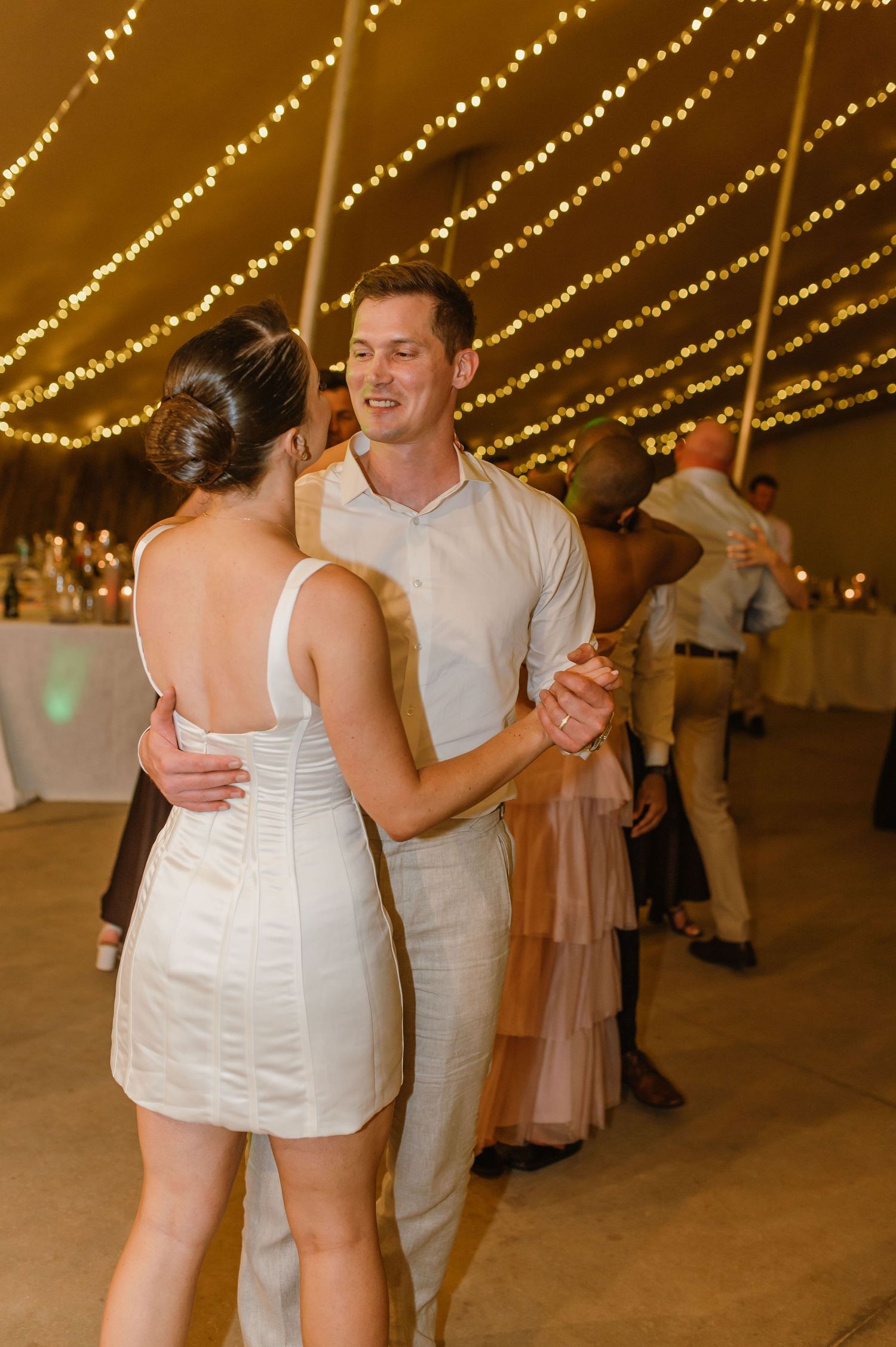 Couples slow dancing on the reception floor under warm string lights.