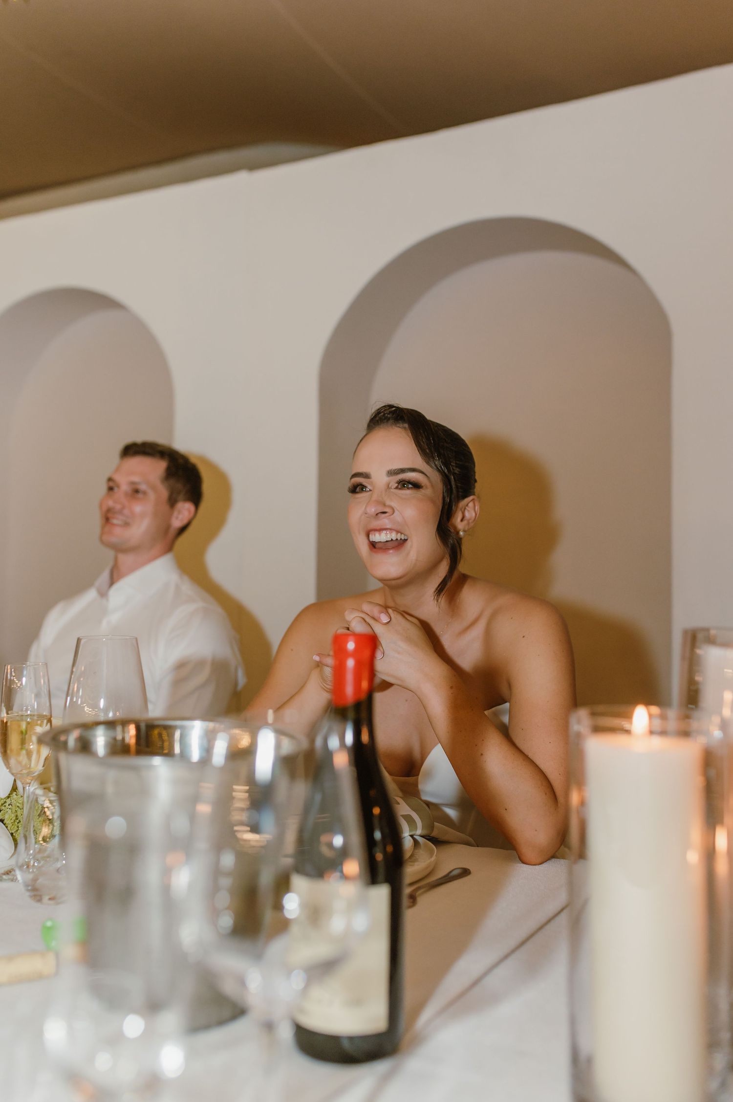 Wedding reception dinner table with white candles and glassware in warm lighting.