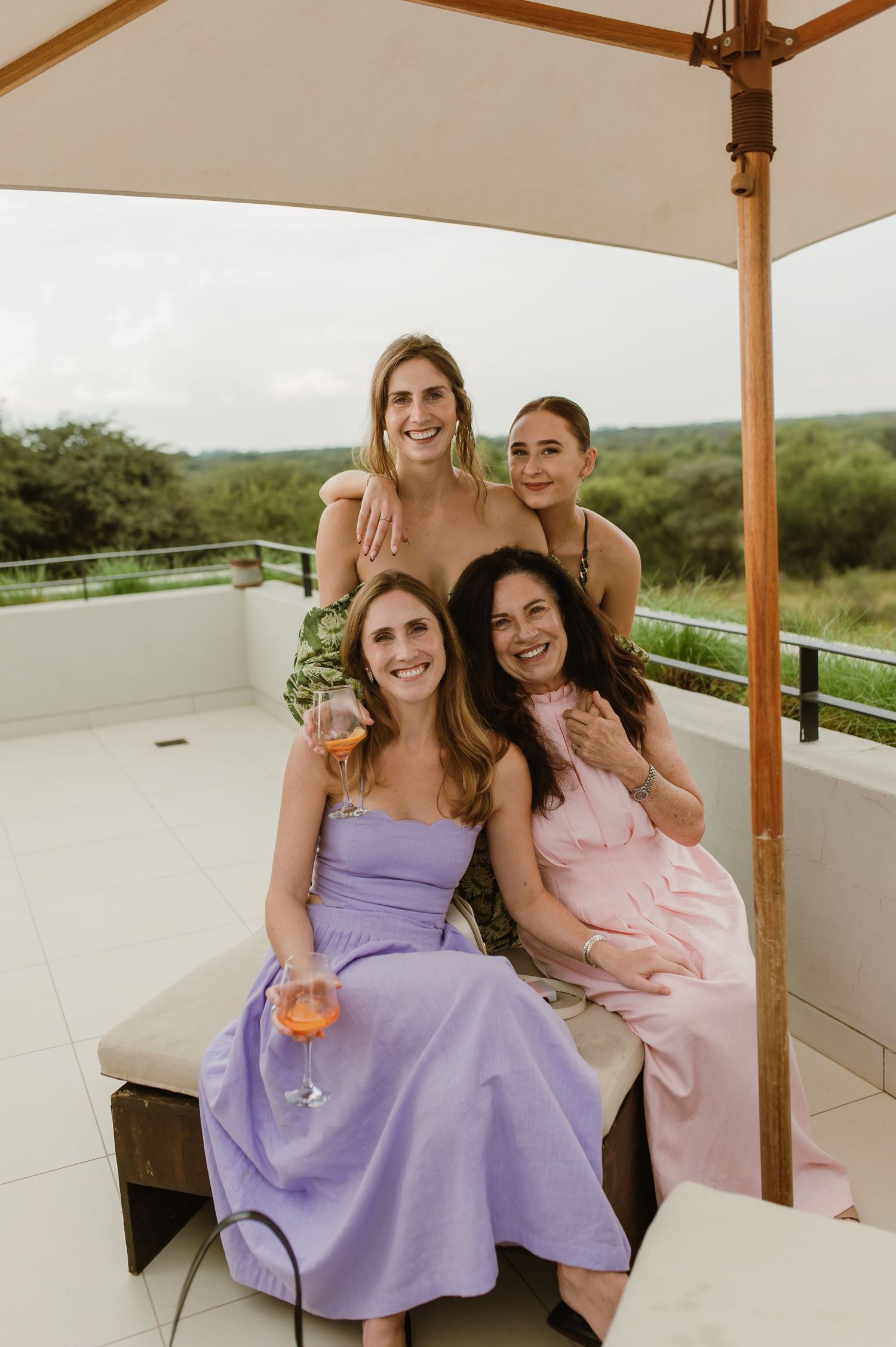 Outdoor celebration on a rooftop terrace with guests in pastel dresses enjoying drinks under an umbrella.