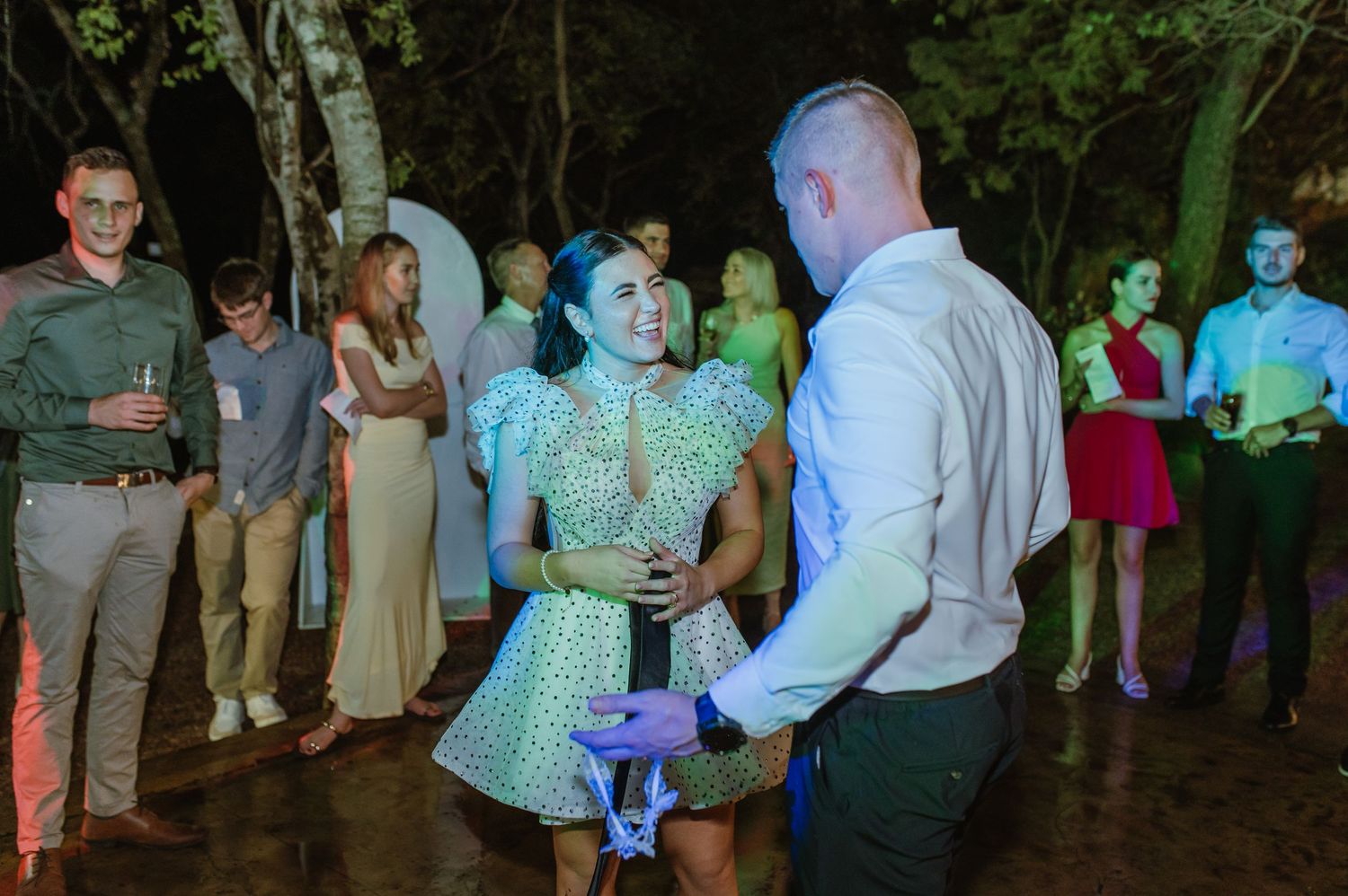 Guests dancing and socializing at an outdoor evening wedding reception under colorful party lights.