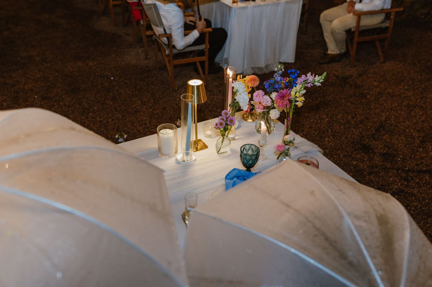 Aerial view of sweetheart table with candles and colorful flowers at outdoor wedding reception.