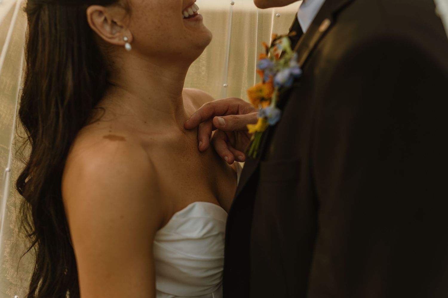 Close-up of laughing bride in strapless gown and groom in suit holding her chin tenderly under her veil.