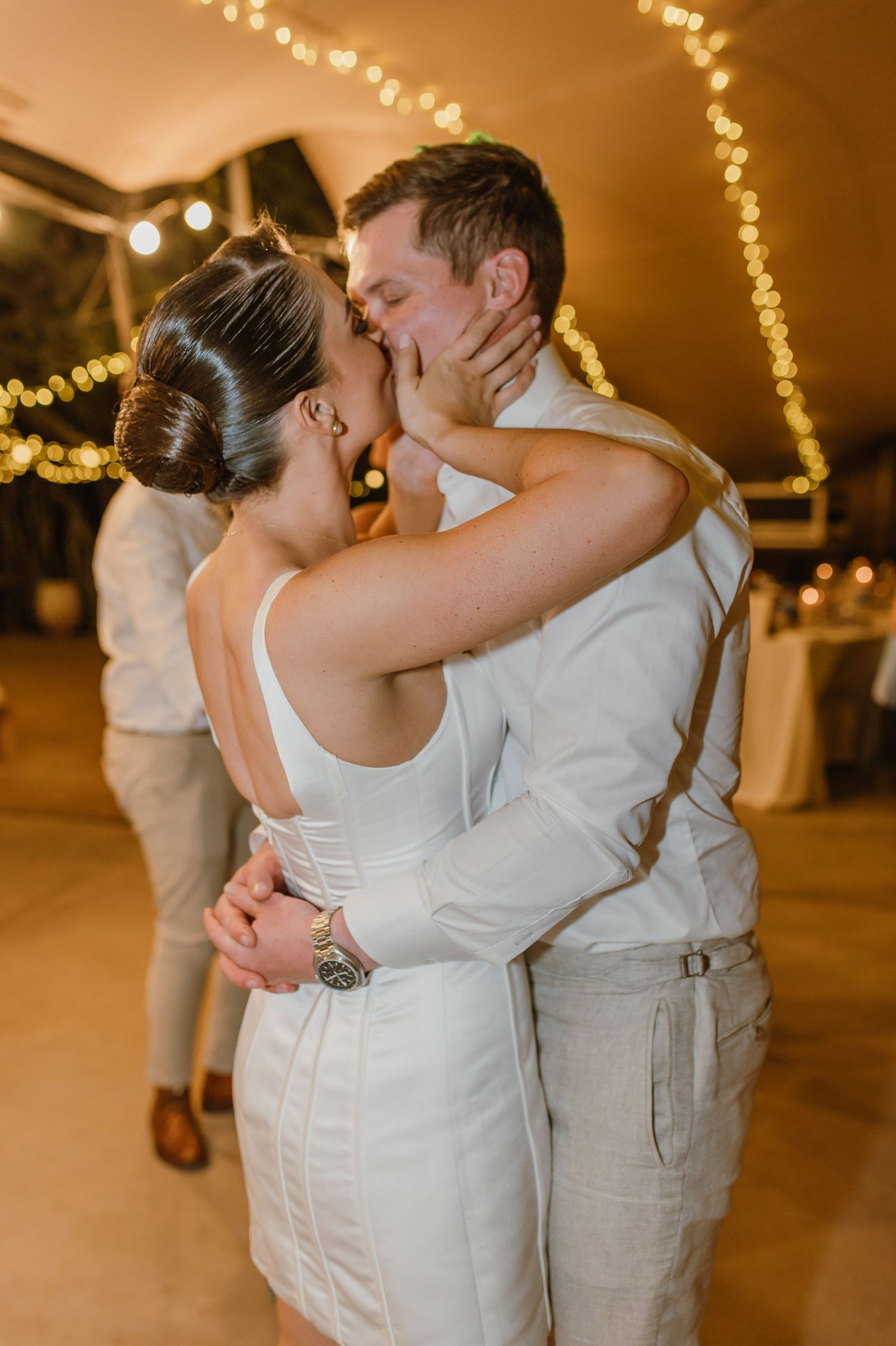 A romantic moment on the dance floor with string lights creating a warm ambiance at a wedding reception.