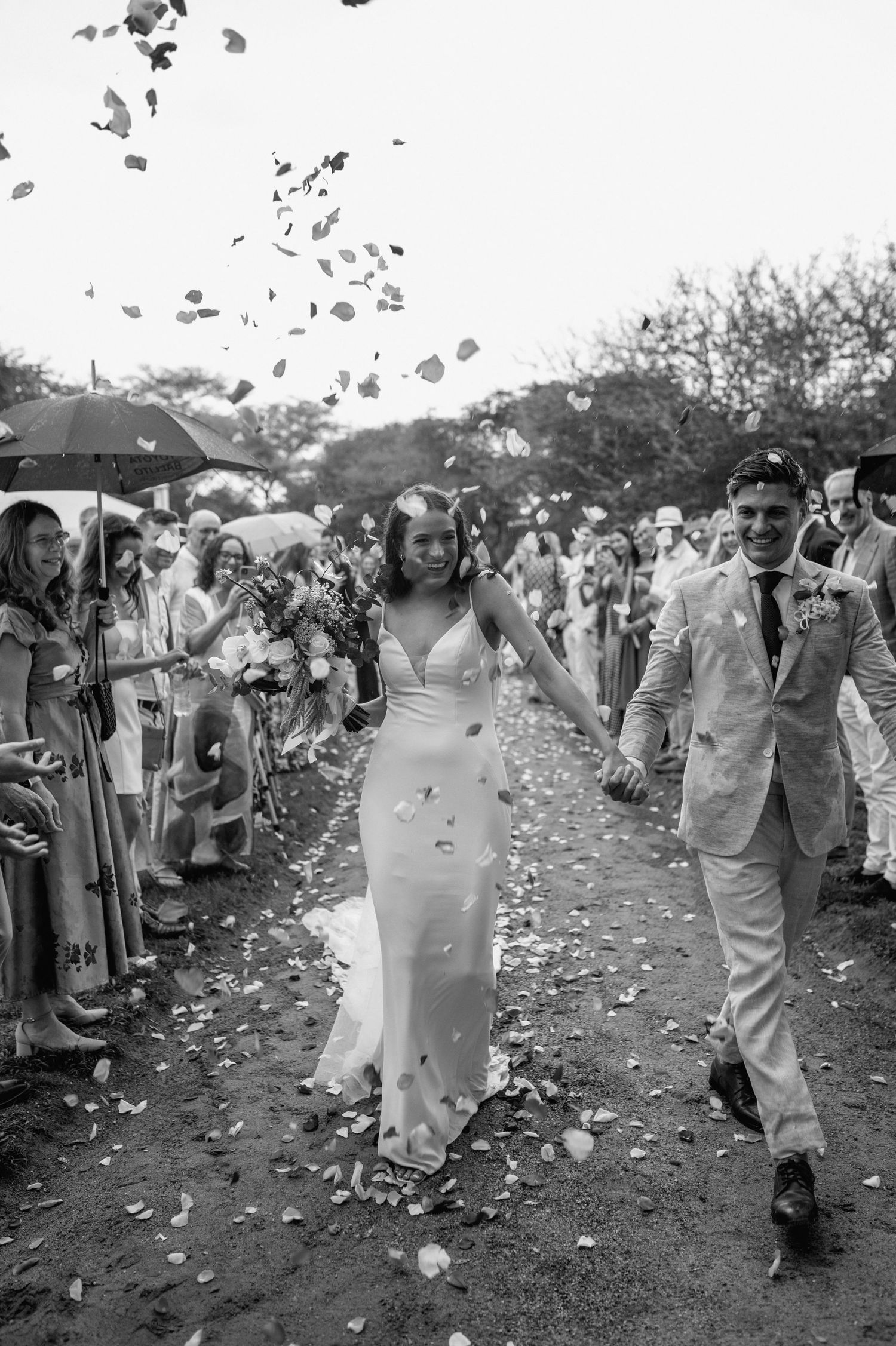 Newlyweds exit ceremony under shower of confetti in black and white photography.