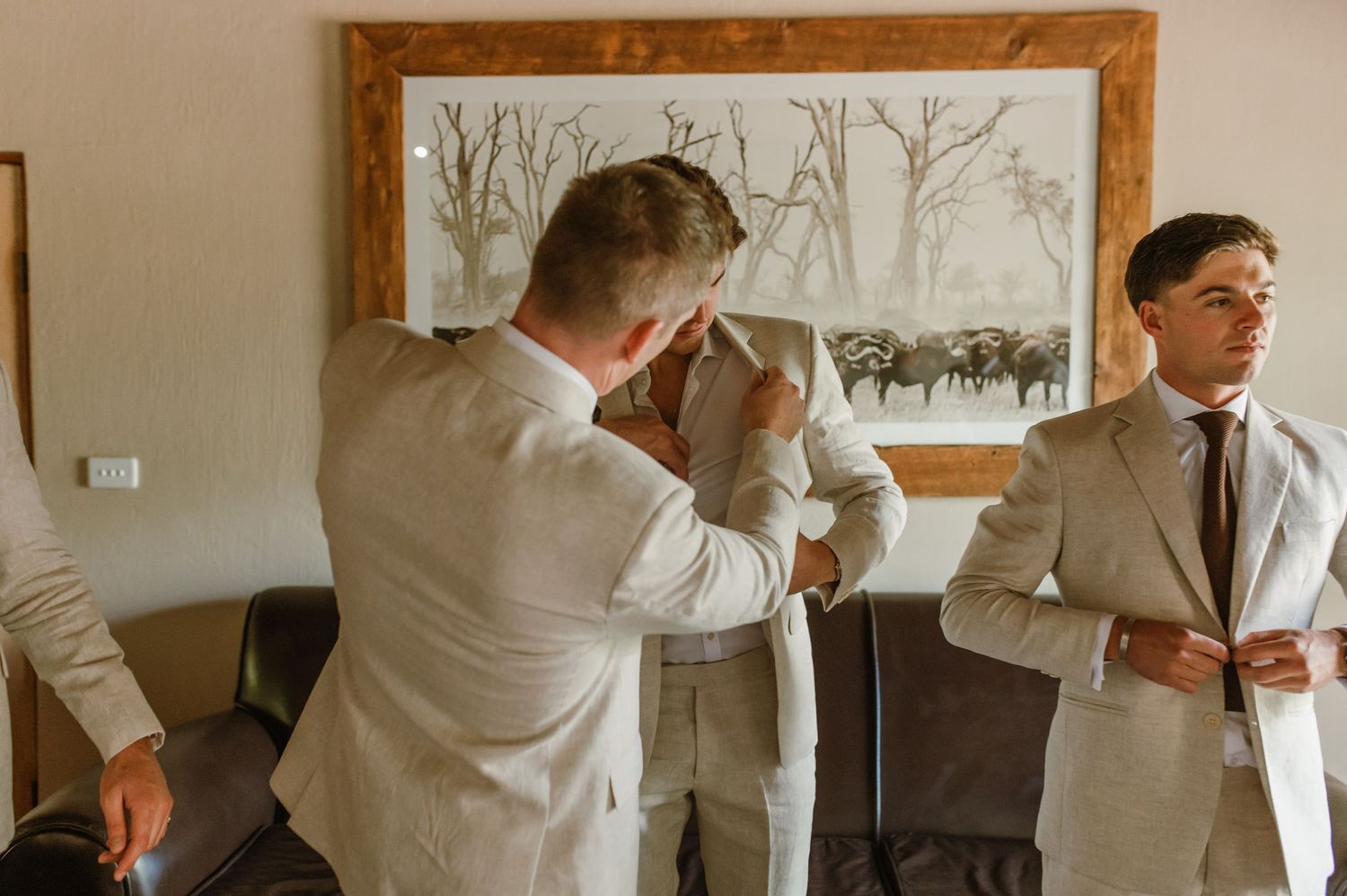 Wedding party members in beige suits pose together in a rustic indoor setting.