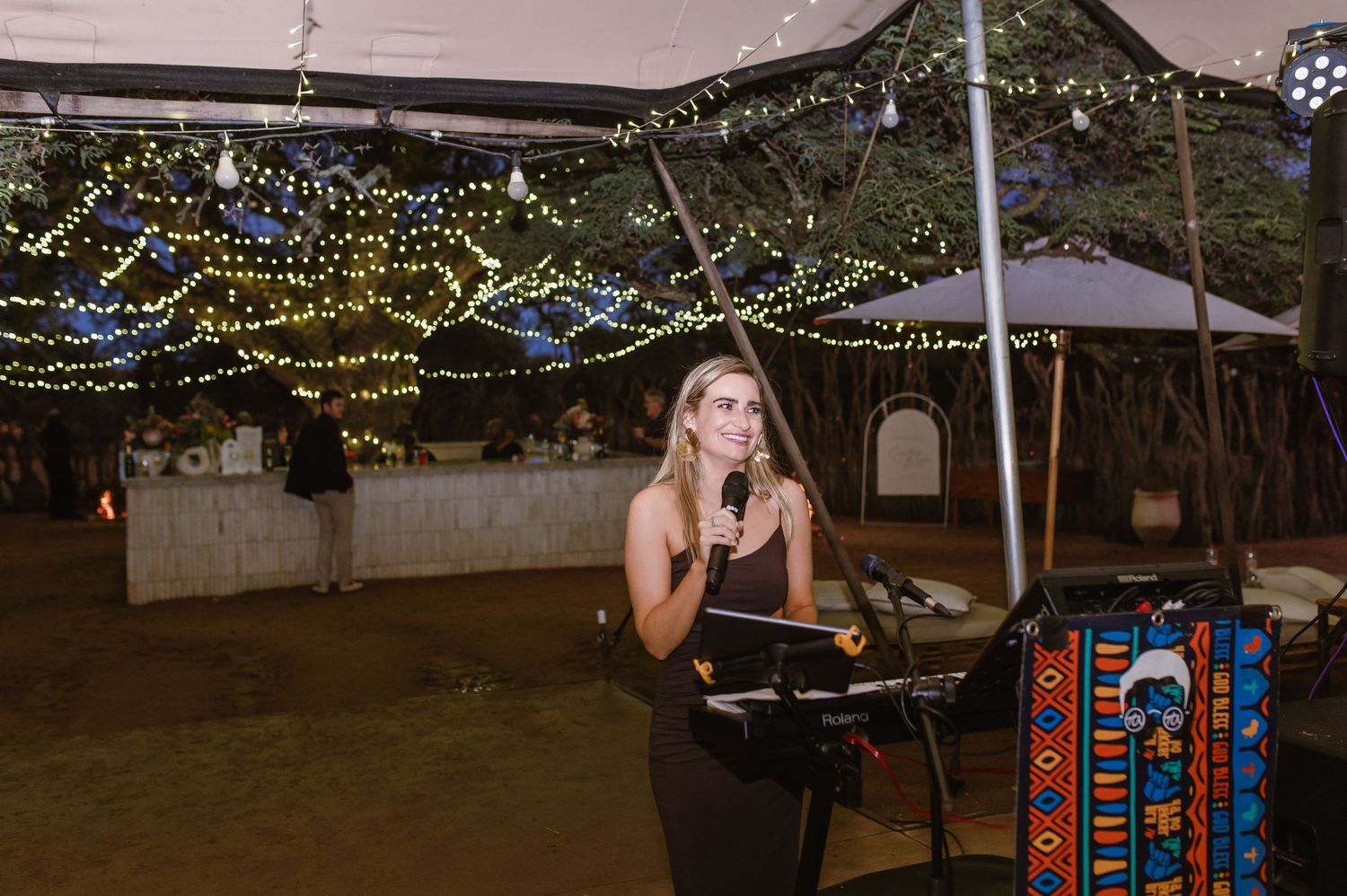 String lights illuminate an outdoor wedding reception area at dusk.