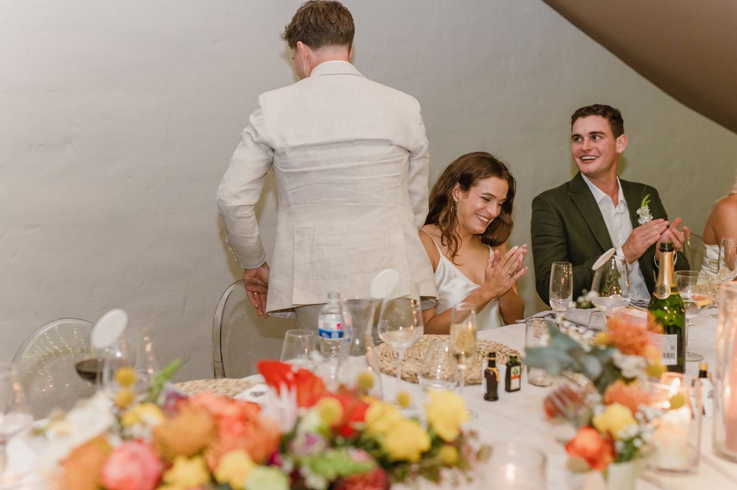 Guests celebrating and clapping during wedding speeches at an elegant indoor reception.