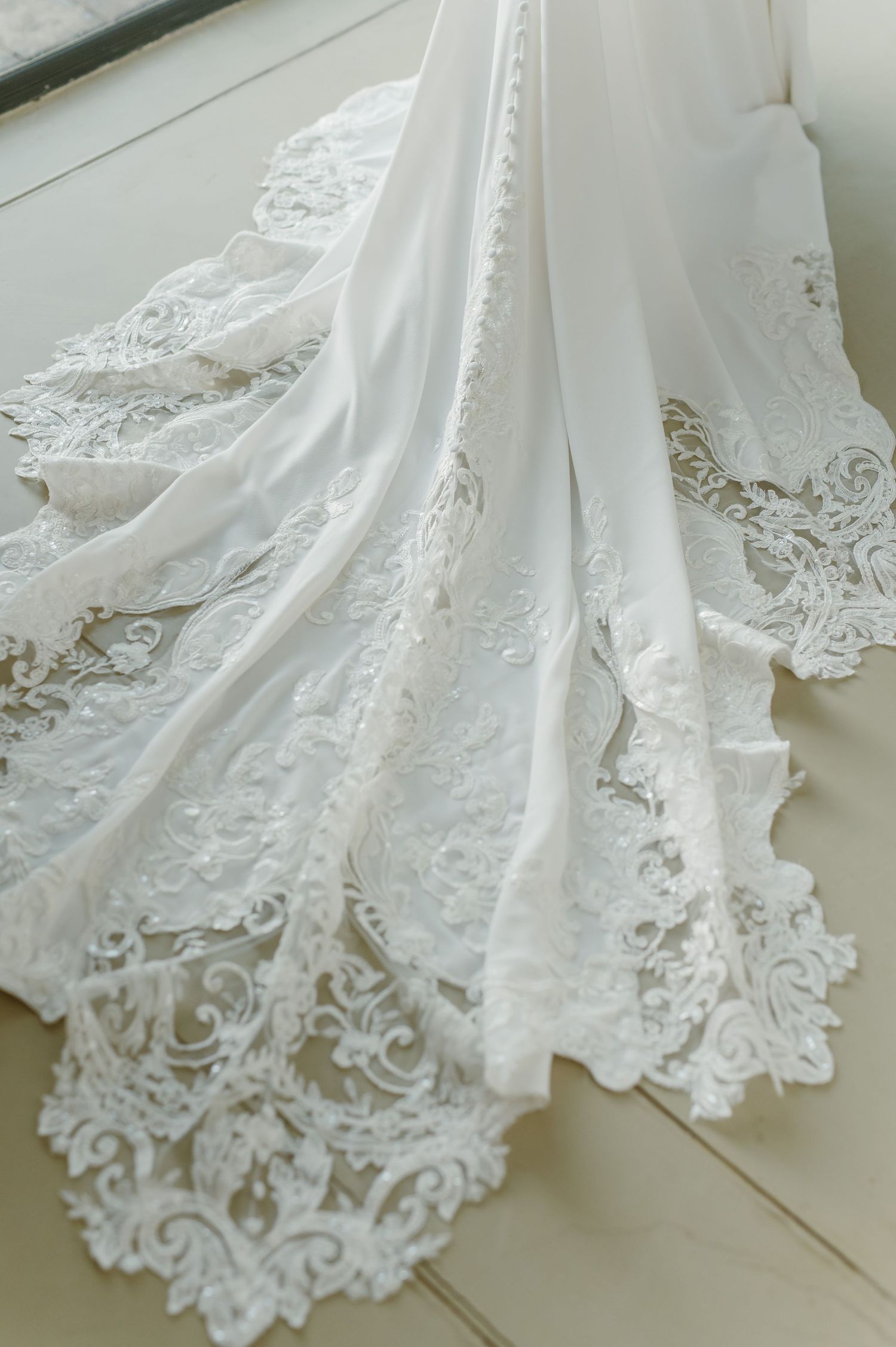 Close-up details of an elegant white wedding dress with intricate lace trim along the bottom.