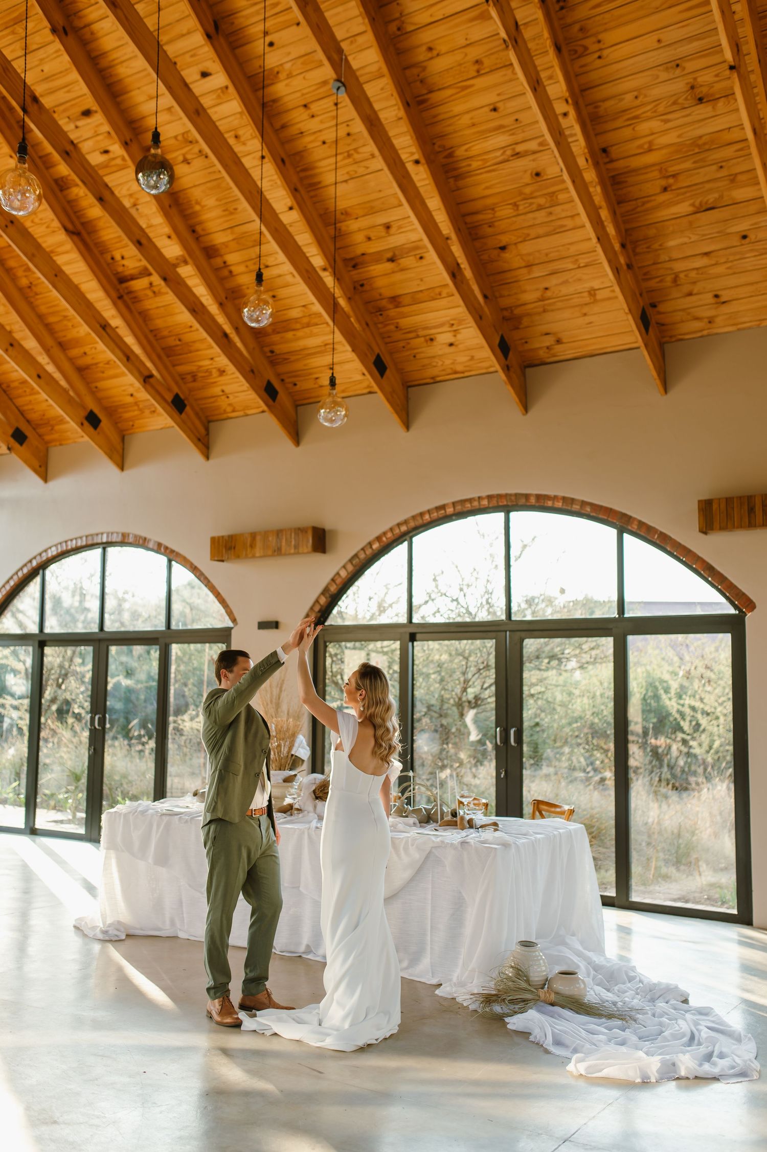 Event space preparation with white-draped tables and wooden beam architecture.