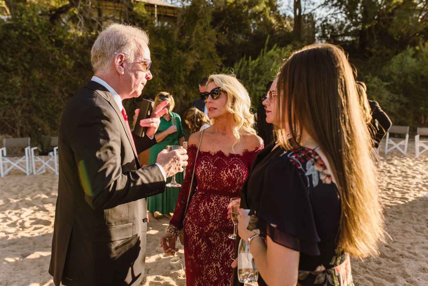 Wedding guests mingle and socialize during an outdoor cocktail hour at sunset on a sandy beach.