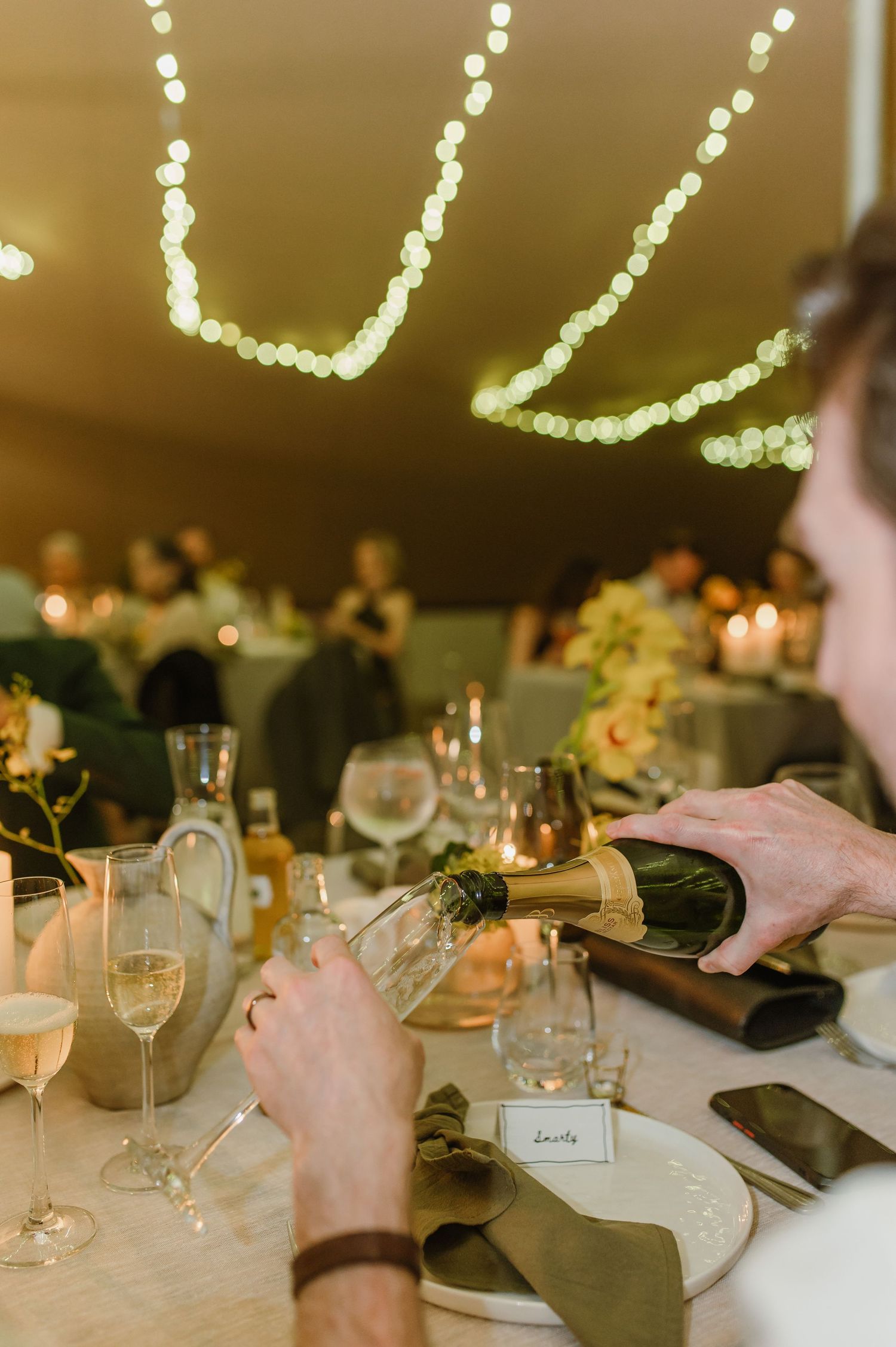 Place settings and wine glasses on elegant table under string lights at wedding reception.