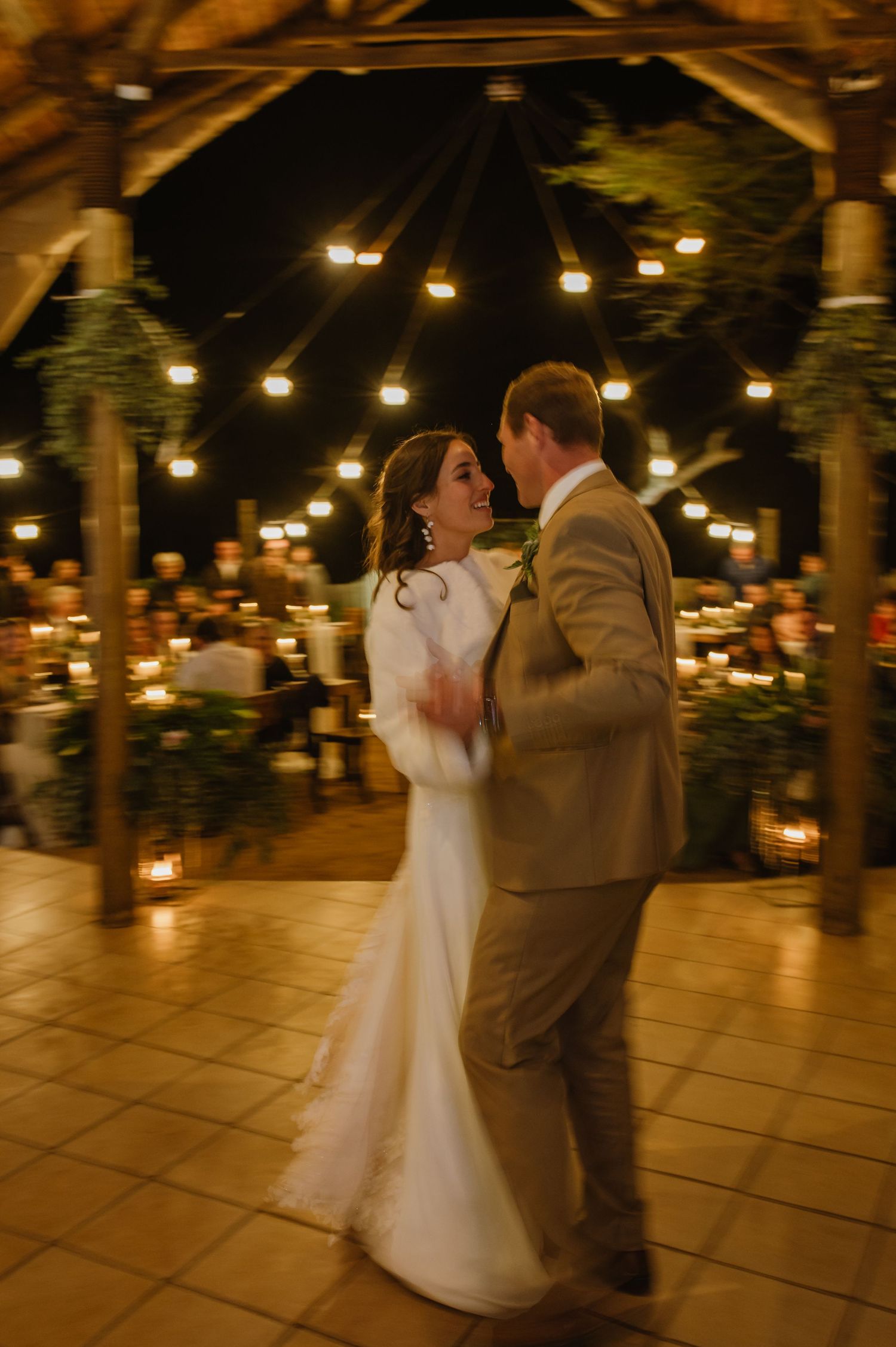 A couple dances under warm string lights at their outdoor wedding reception.