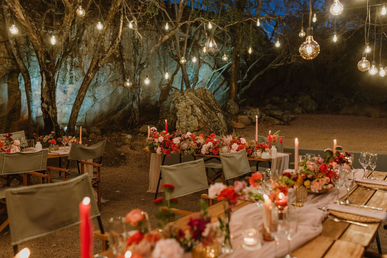 Romantic outdoor wedding reception setup with hanging lights and floral decorations.