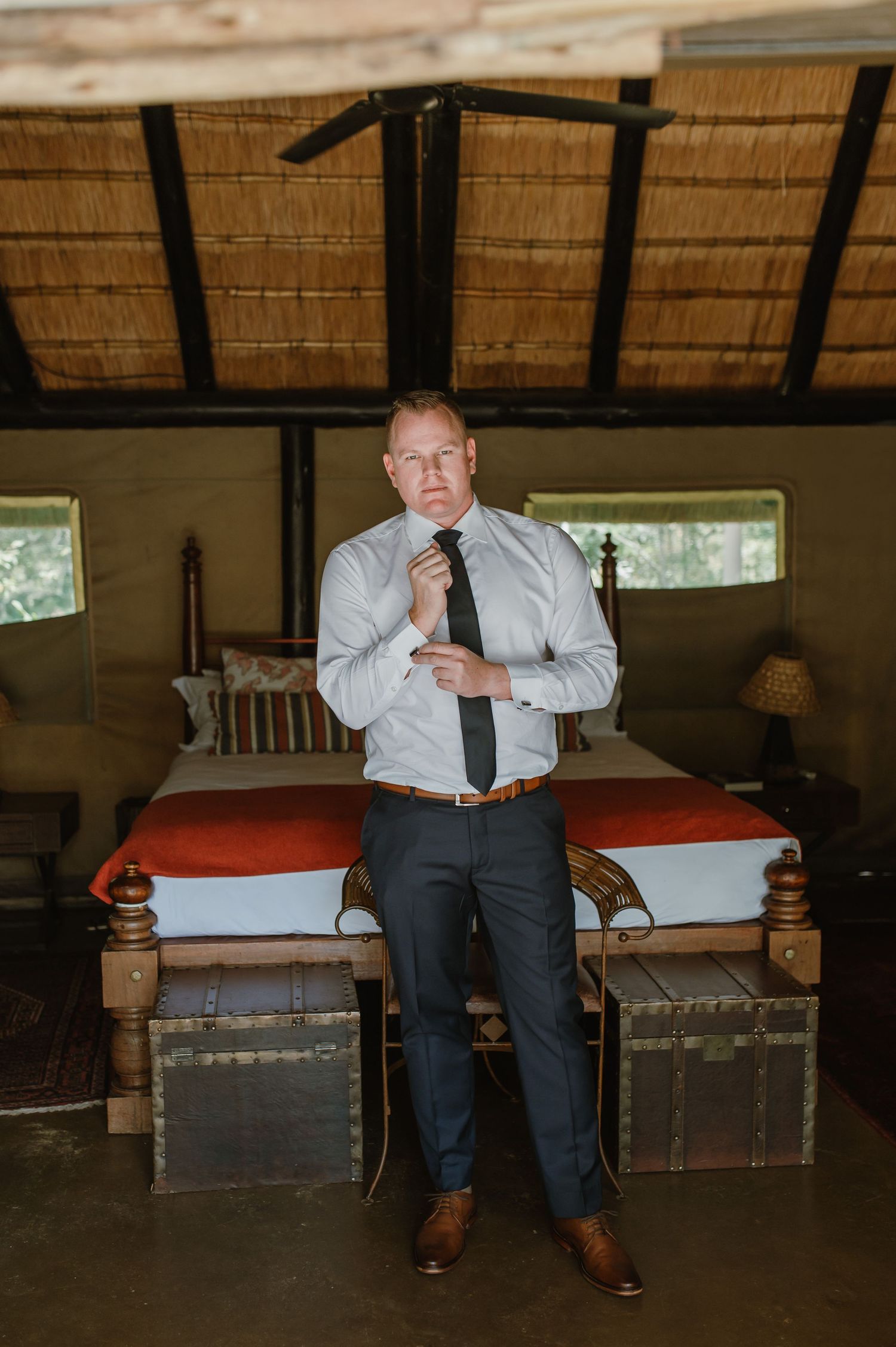 Person in formal attire sitting on wooden furniture in a rustic room with thatched roof.