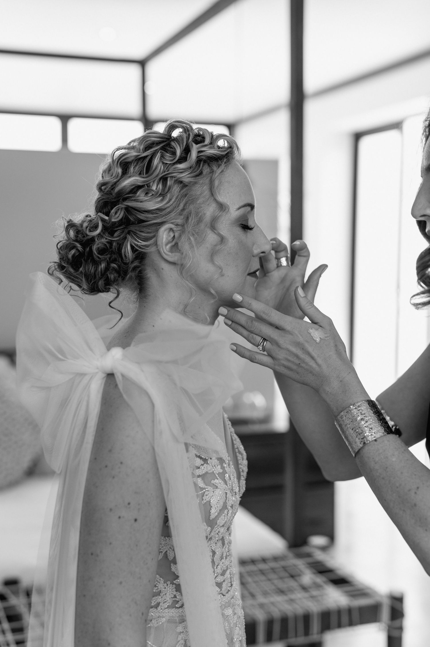 A bride getting her makeup applied in a bright white room.