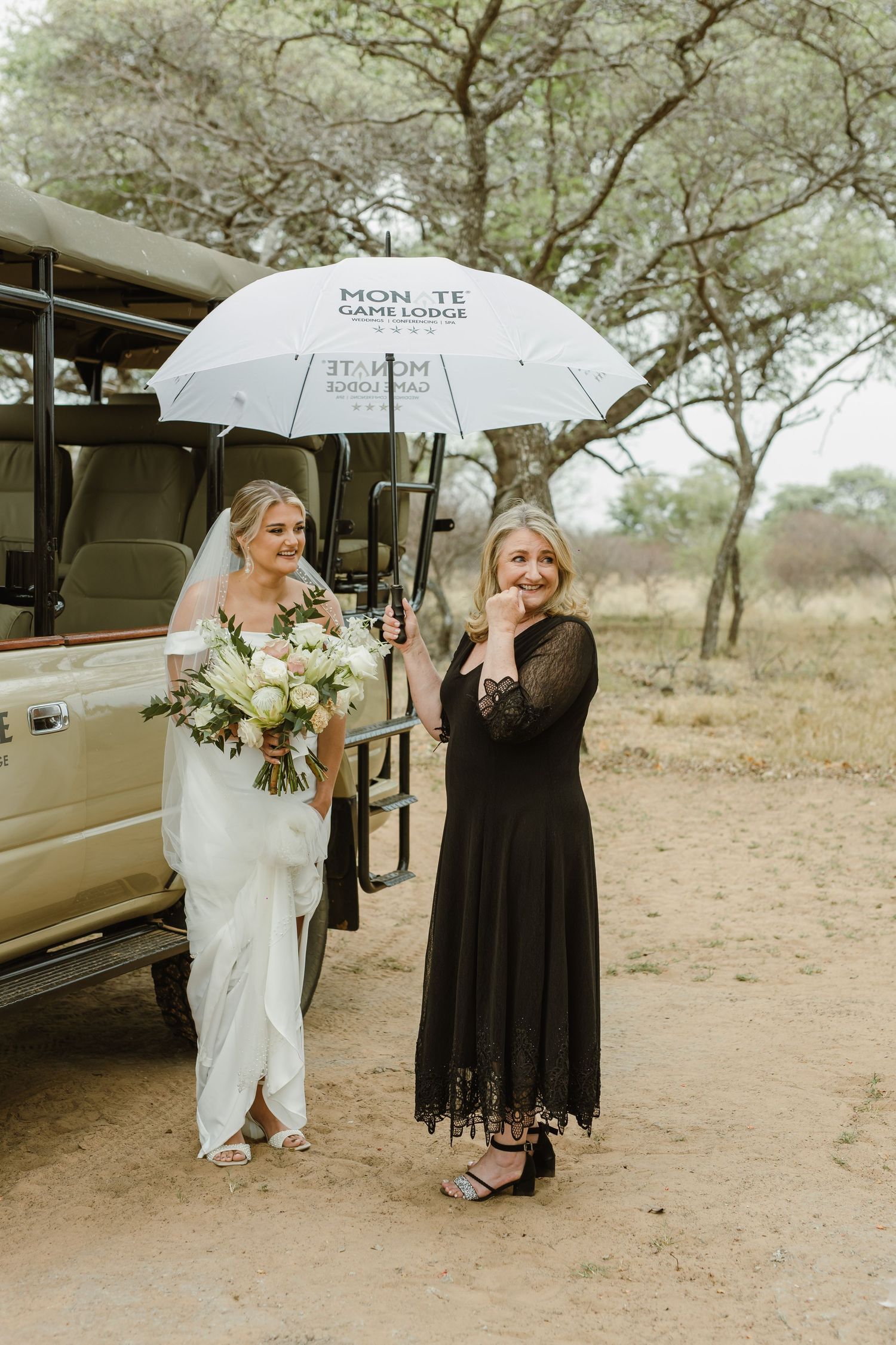 Wedding group stands with white umbrellas against a natural desert landscape backdrop.