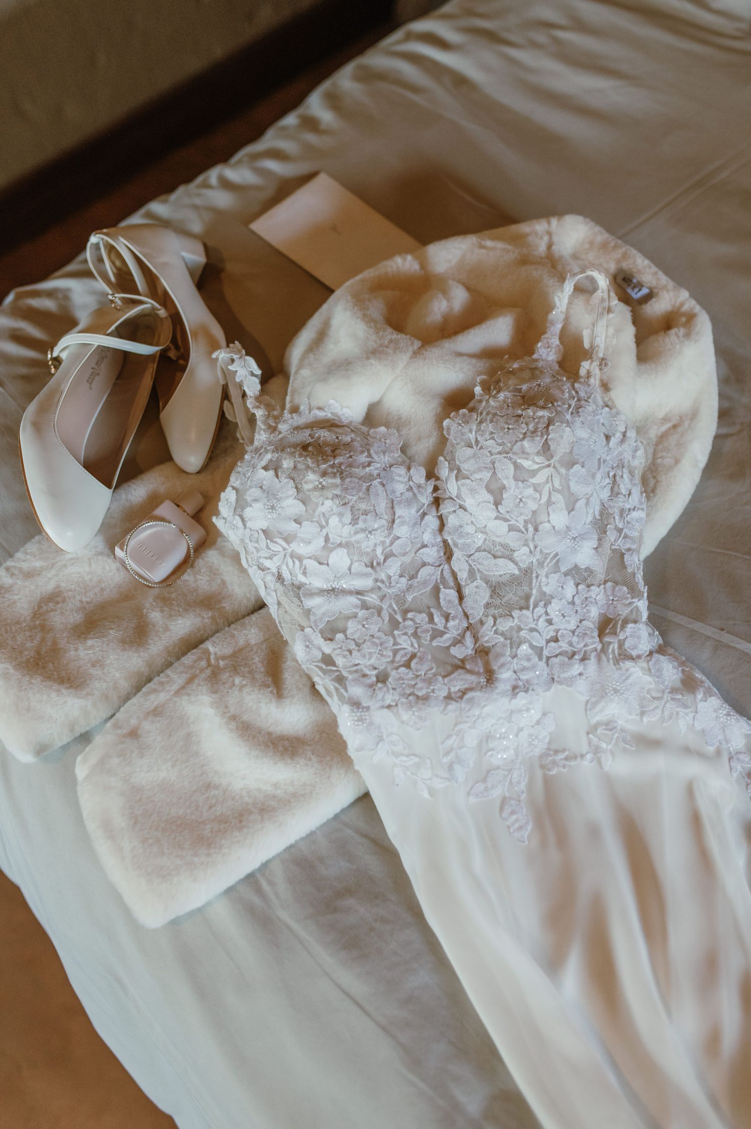 A delicate white wedding dress with lace detailing lies flat on a cream-colored surface.