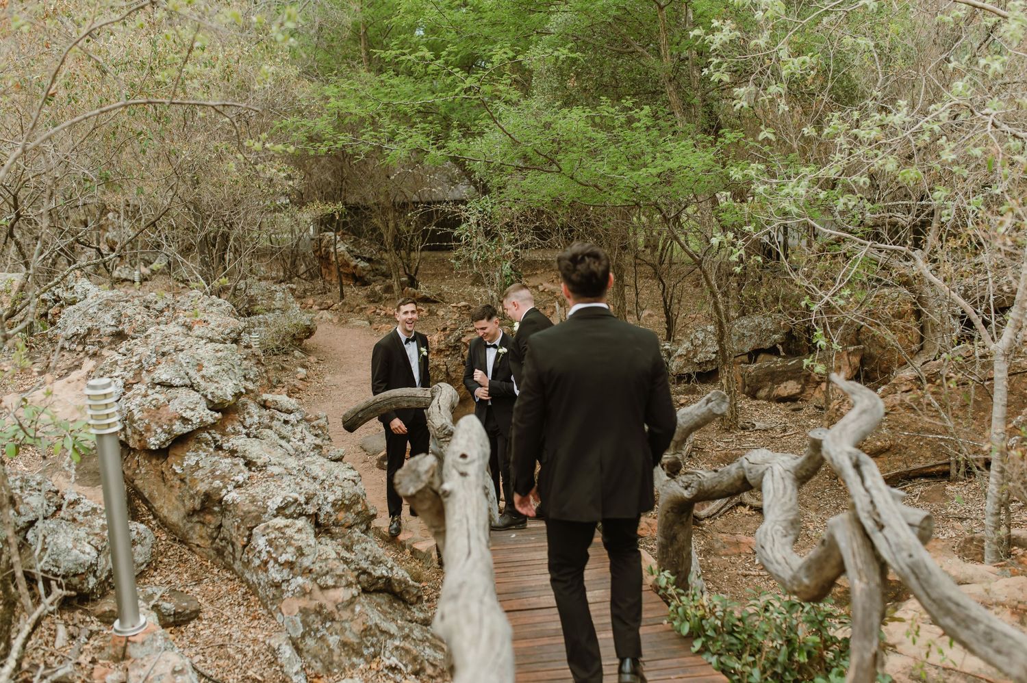 Wedding party members gather on a natural path surrounded by greenery and rocks.