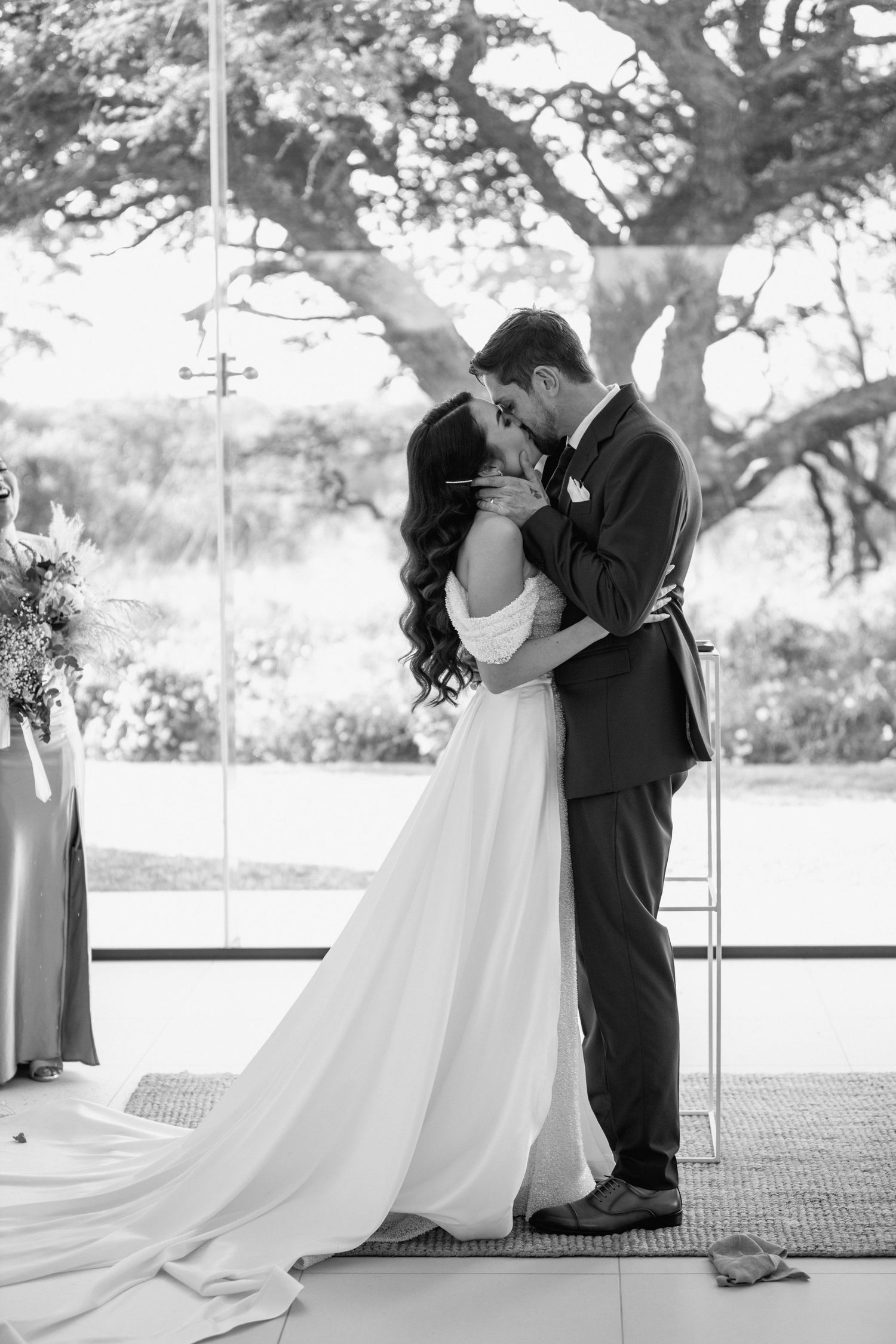 Romantic black and white wedding portrait with couple embracing under trees.