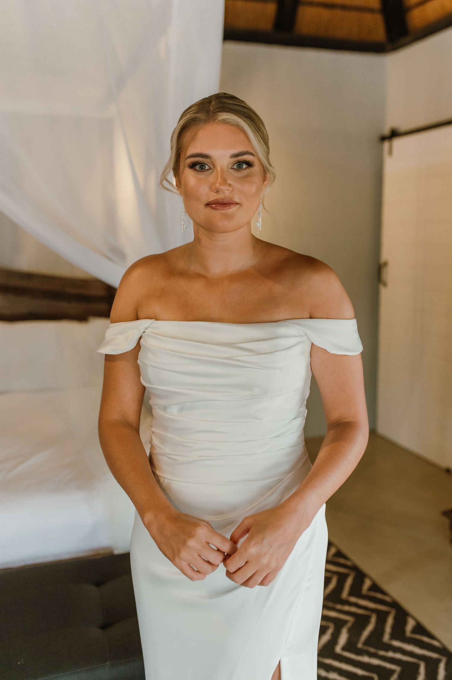 Final adjustments of a classic white off-shoulder wedding dress.