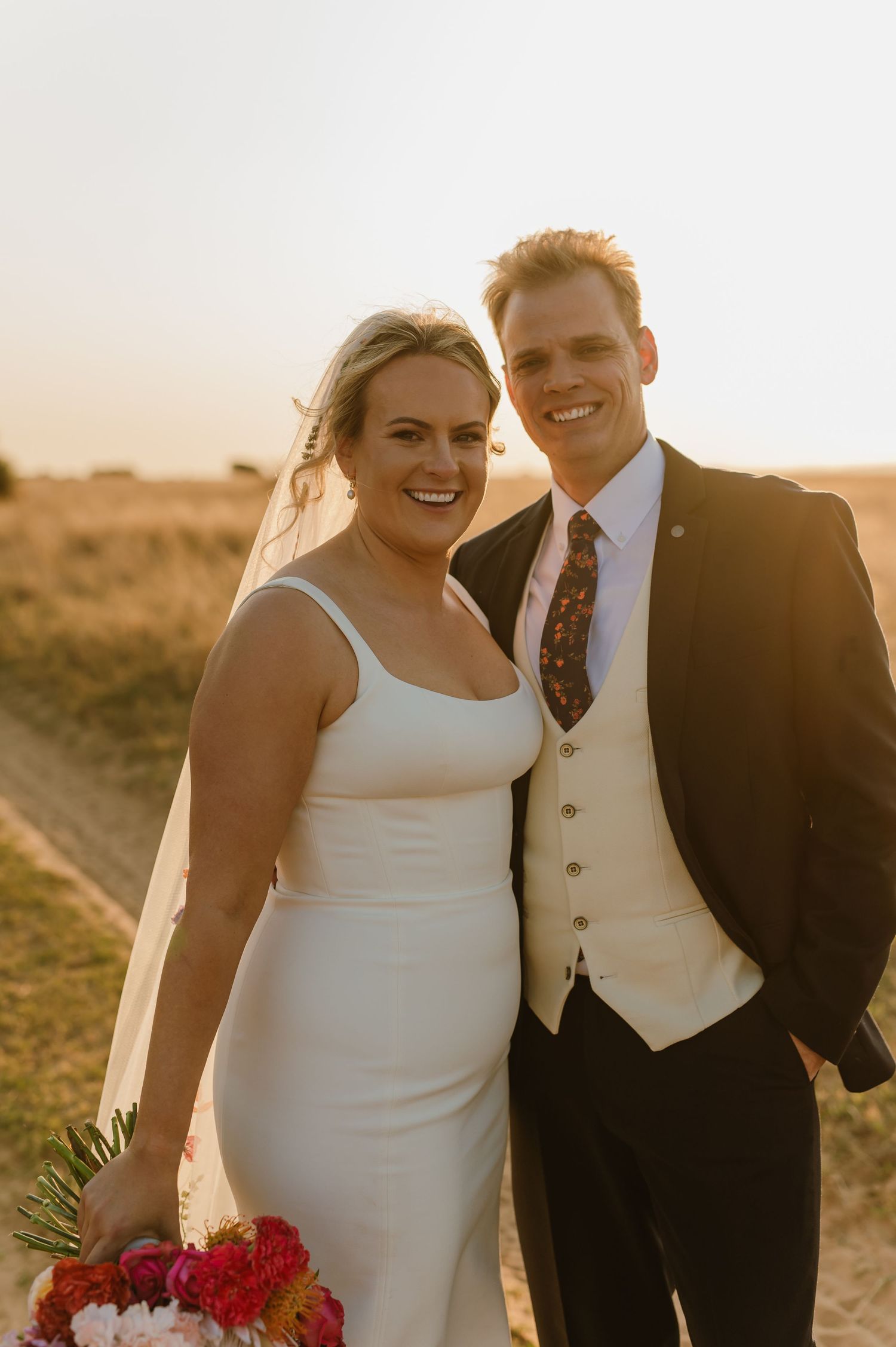 A happy couple poses for wedding photos in a field during golden hour.