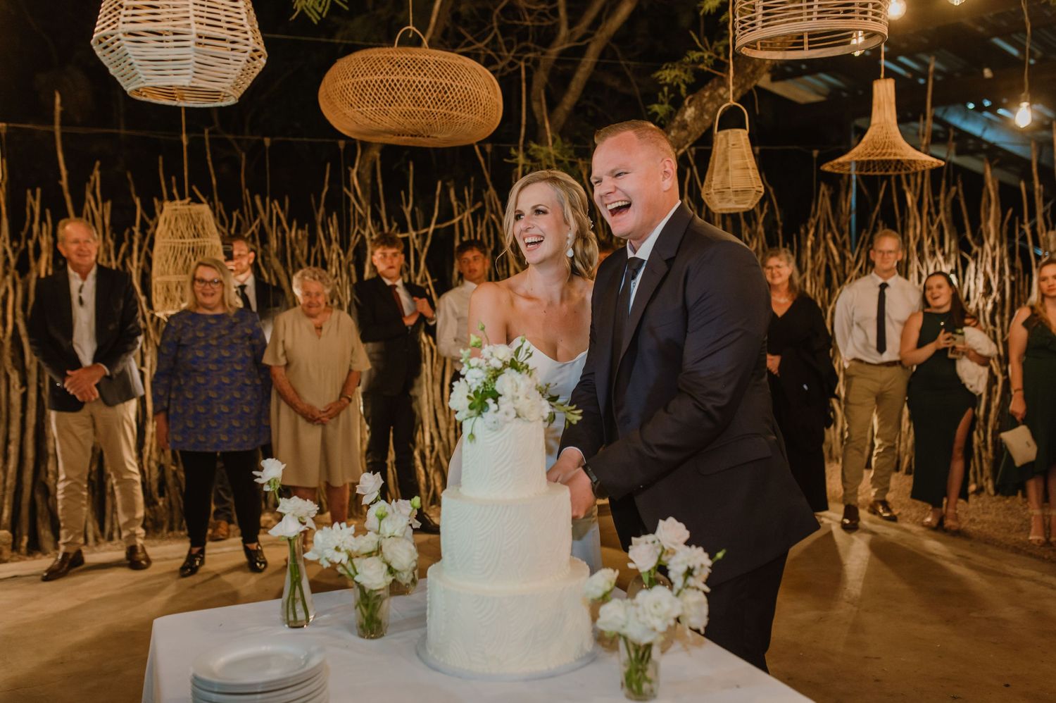 Elegant wedding reception setup with white floral centerpieces and rattan lighting in an outdoor venue.