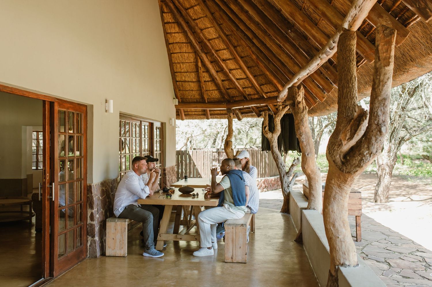 Safari lodge veranda with thatched roof and natural stone pillars in afternoon light.
