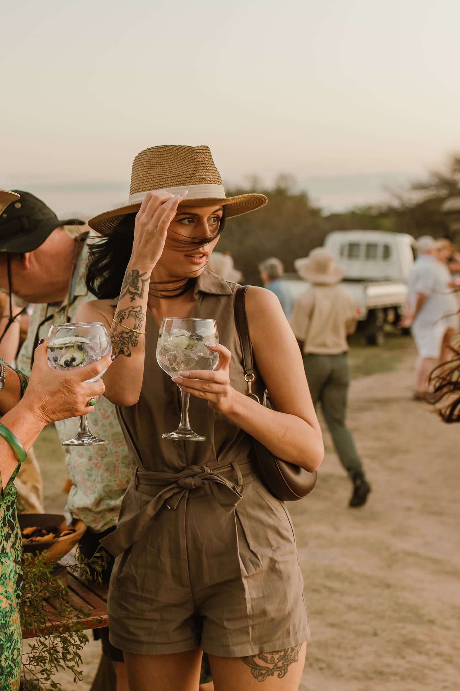 People in casual attire enjoying wine glasses at an outdoor sunset event.