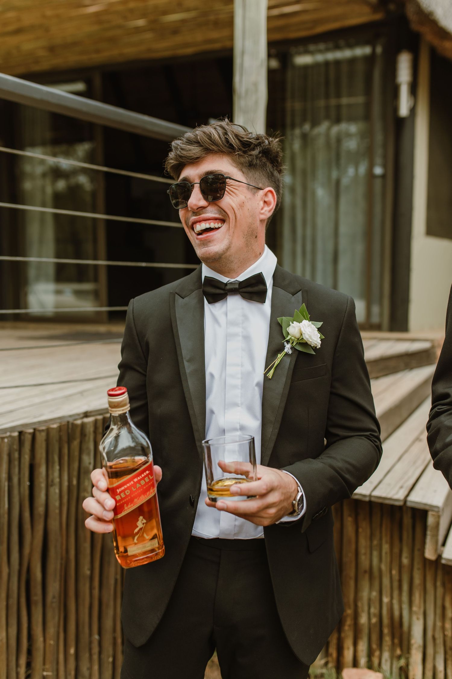 Wedding party members in formal attire enjoying drinks and conversation outdoors.