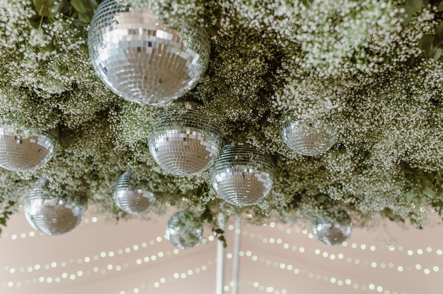 Twinkling string lights create a magical ceiling display at an indoor wedding reception.