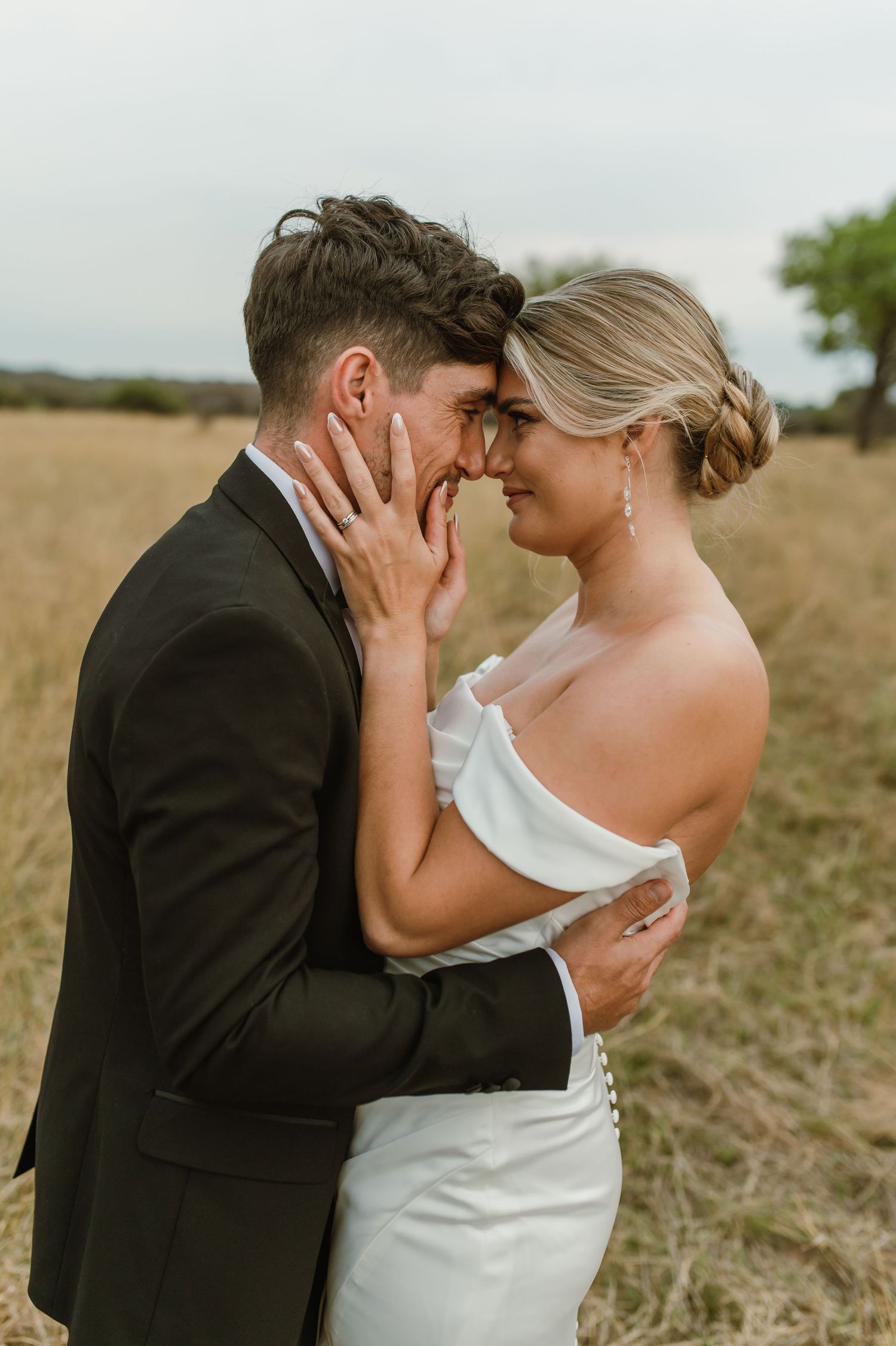 An intimate wedding portrait shows a couple embracing in a rustic outdoor setting.