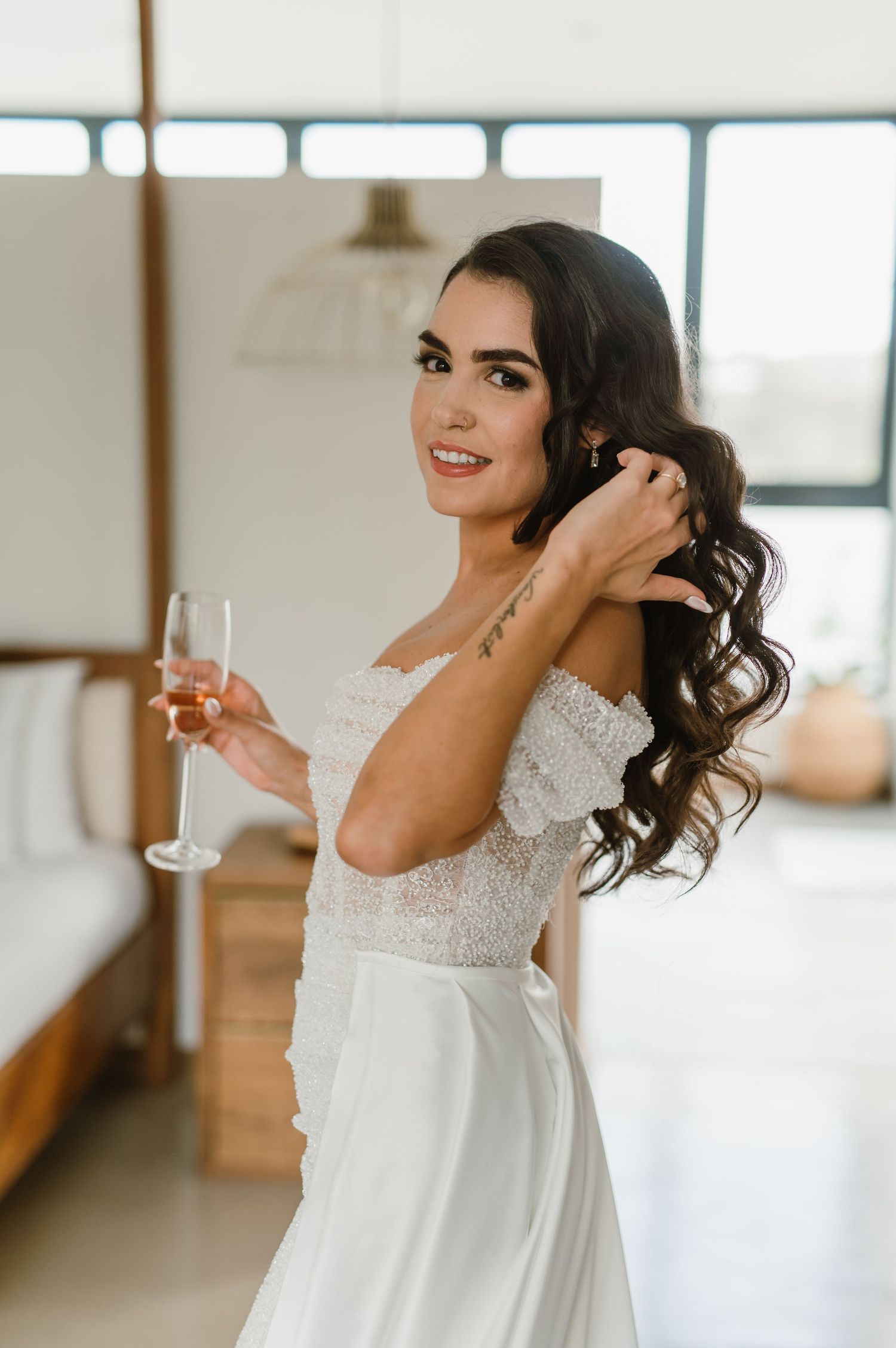 Elegant bride in a white off-shoulder wedding dress poses joyfully in a bright modern space.