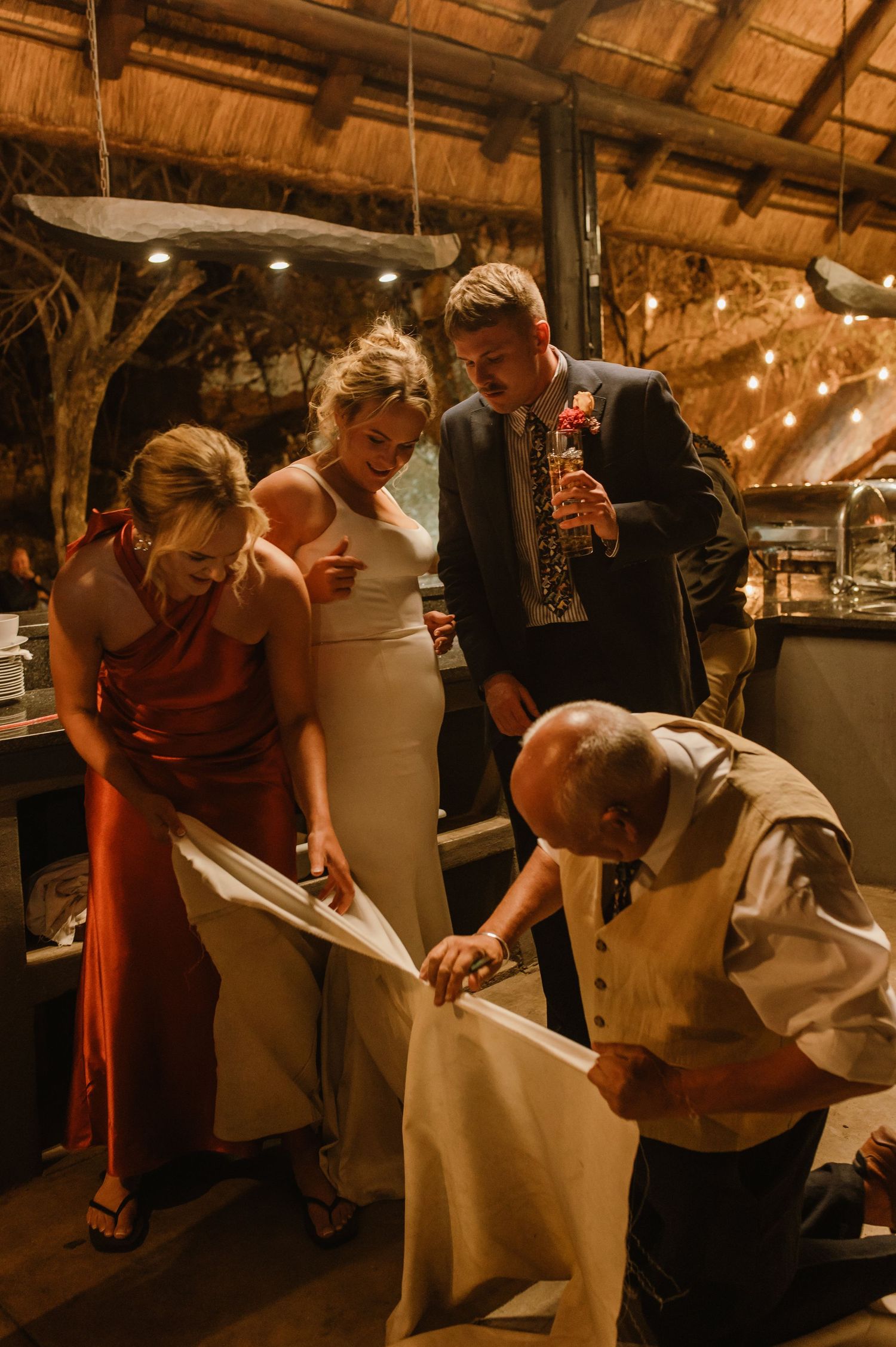 Wedding party members help arrange a white wedding dress at an evening reception.