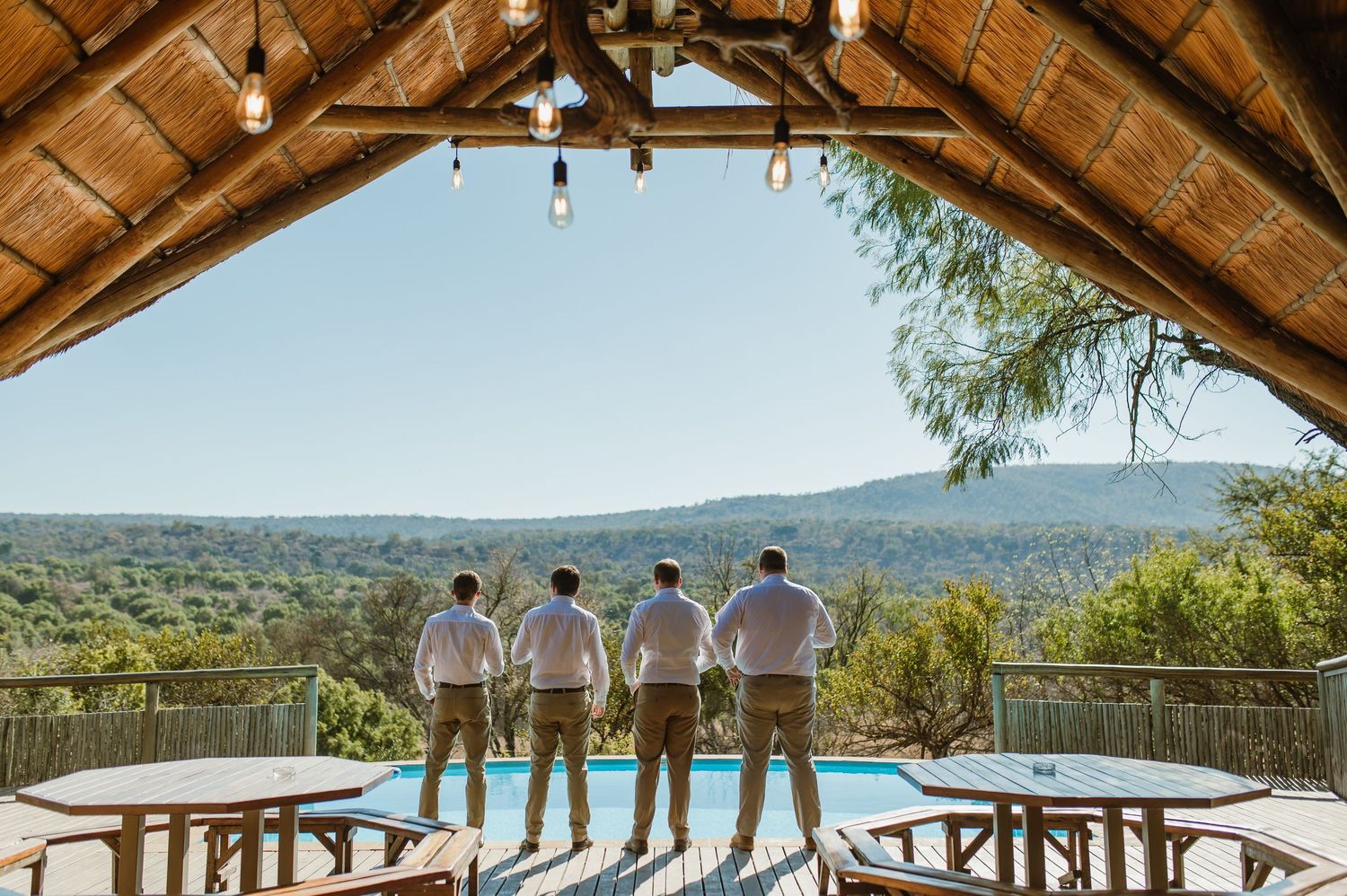 Groomsmen standing on deck overlooking scenic mountain valley and swimming pool.