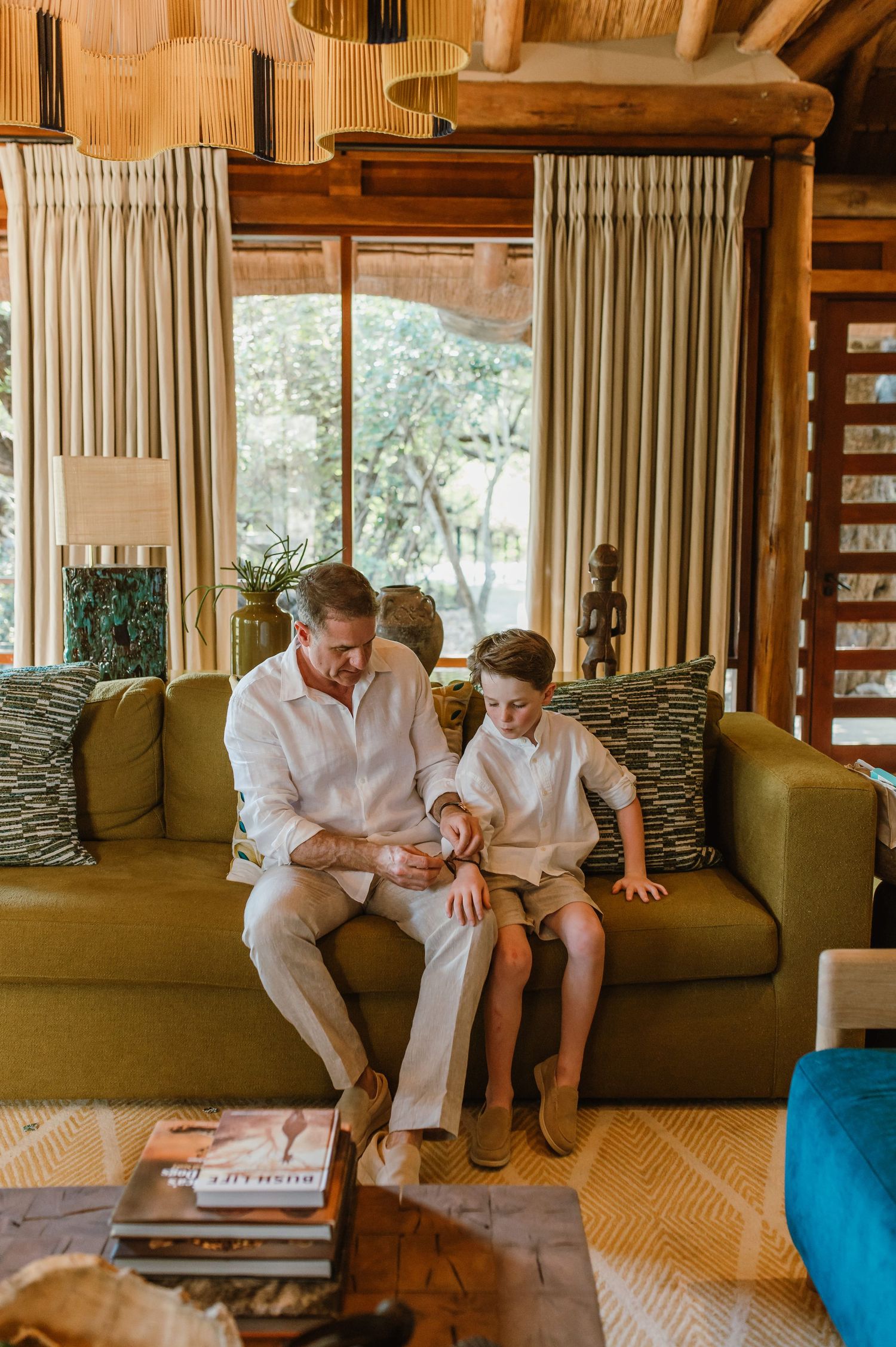 Father and son sitting together on a green sofa in a rustic lodge interior.