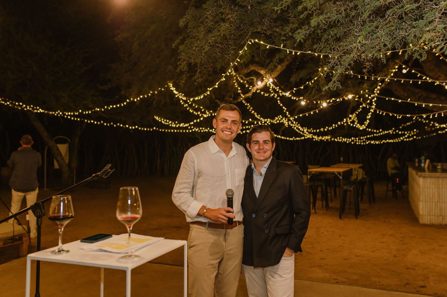 Two guests pose together at an evening outdoor event with string lights overhead.