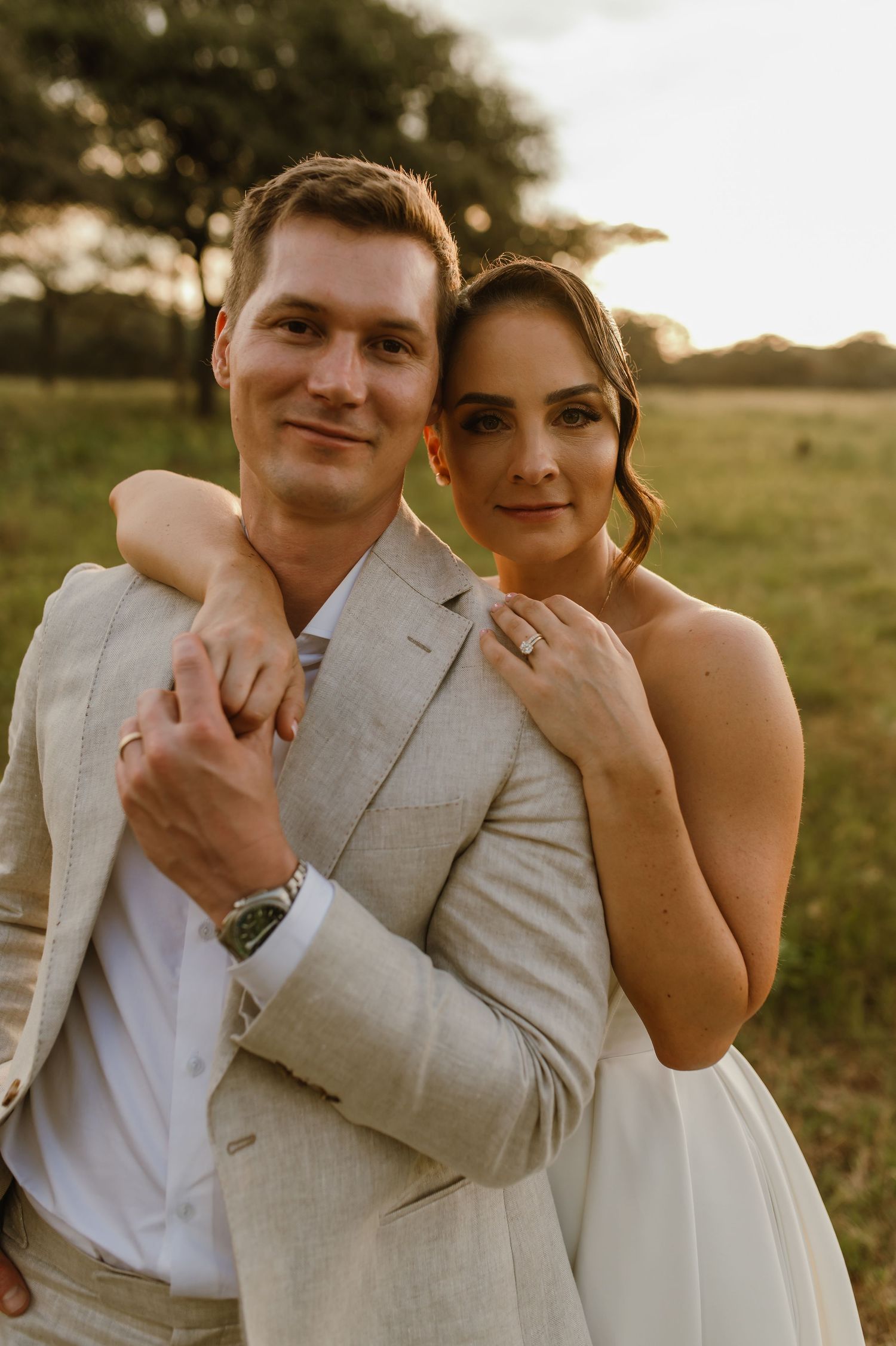 A romantic wedding portrait captured in warm golden light against a natural outdoor backdrop.