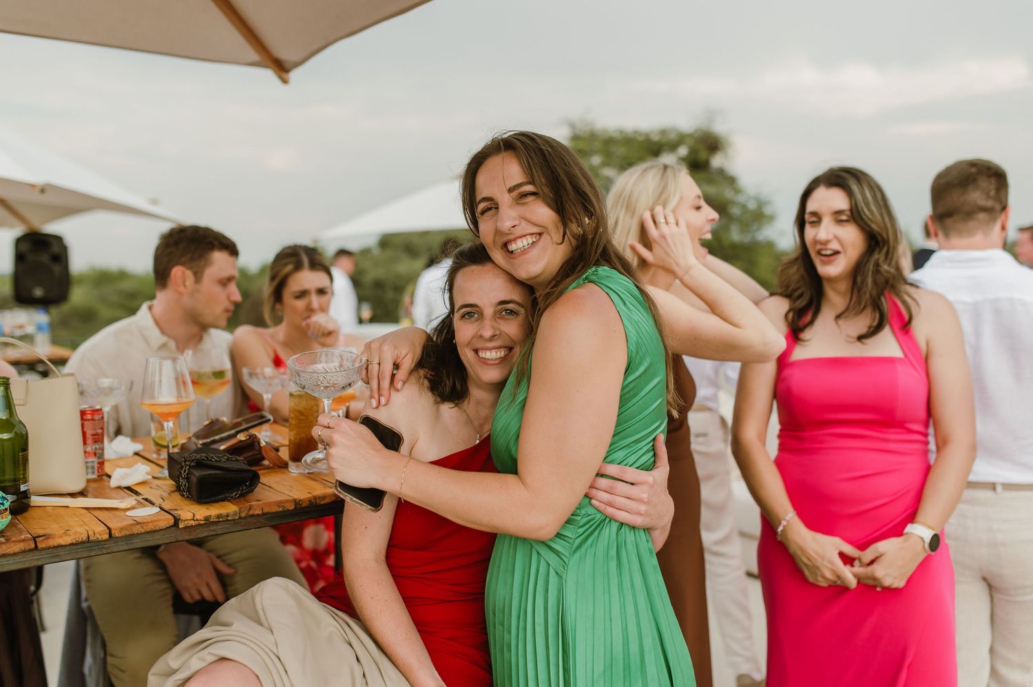 Wedding party members in vibrant dresses share joyful moments during an outdoor celebration.