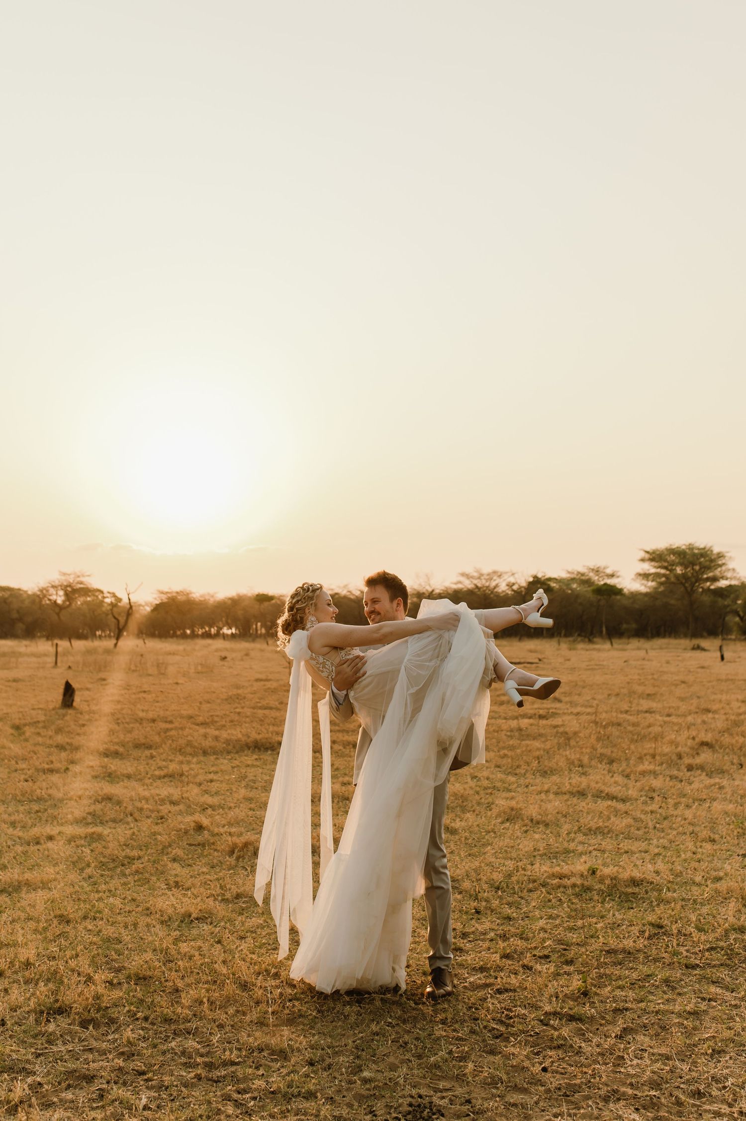 A couple dances together in a golden sunlit field at sunset wearing wedding attire.