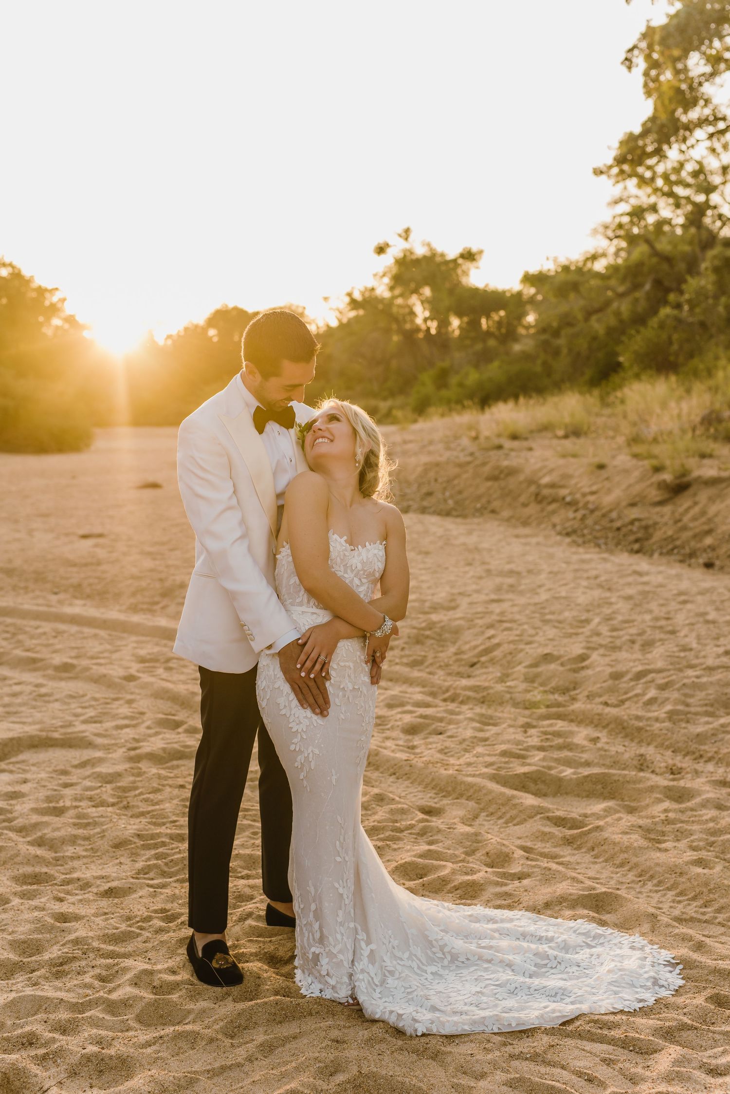 Elegant wedding portrait on sandy beach during golden hour sunset.