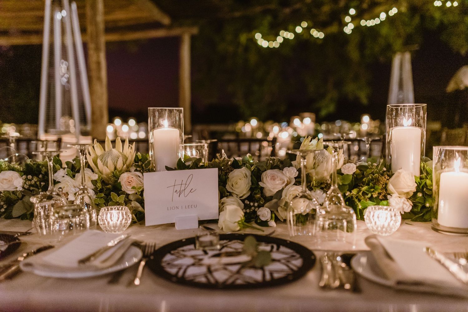 Close-up of romantic table decor with taper candles, greenery garlands and delicate place settings.