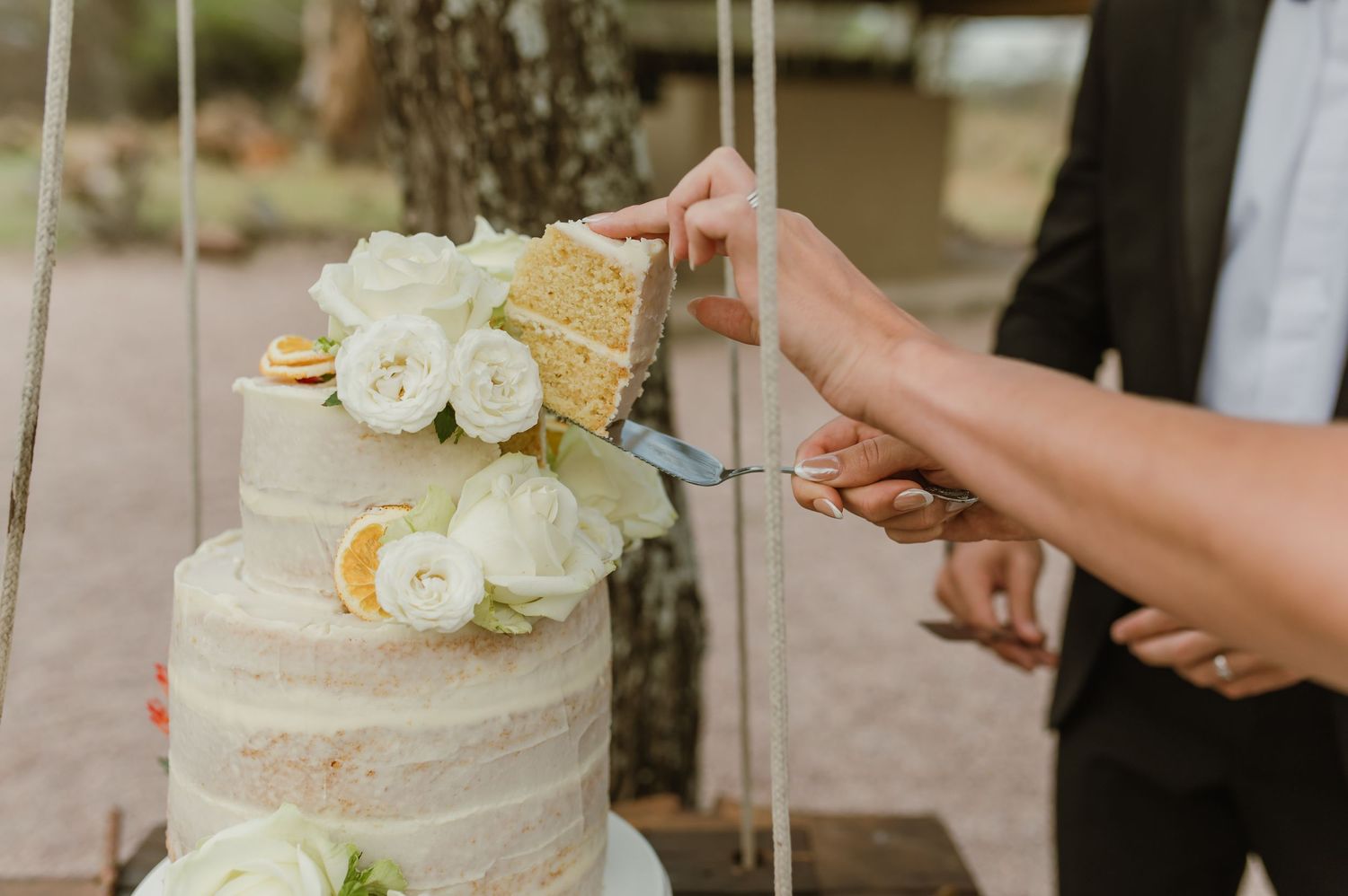 Wedding cake display with white frosting and citrus decorations at outdoor venue.