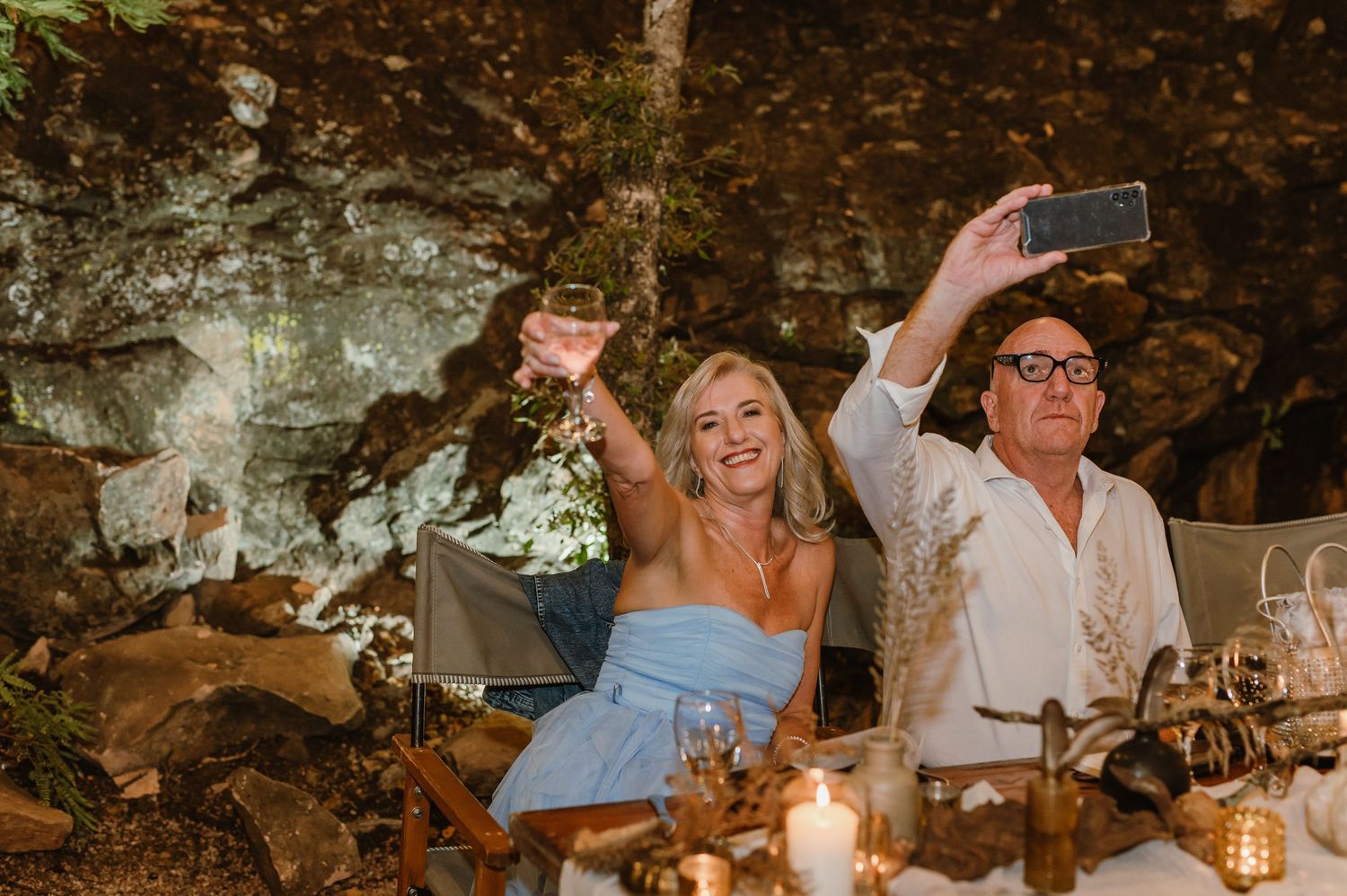Wedding guests raise their glasses in celebration at an outdoor reception dinner.