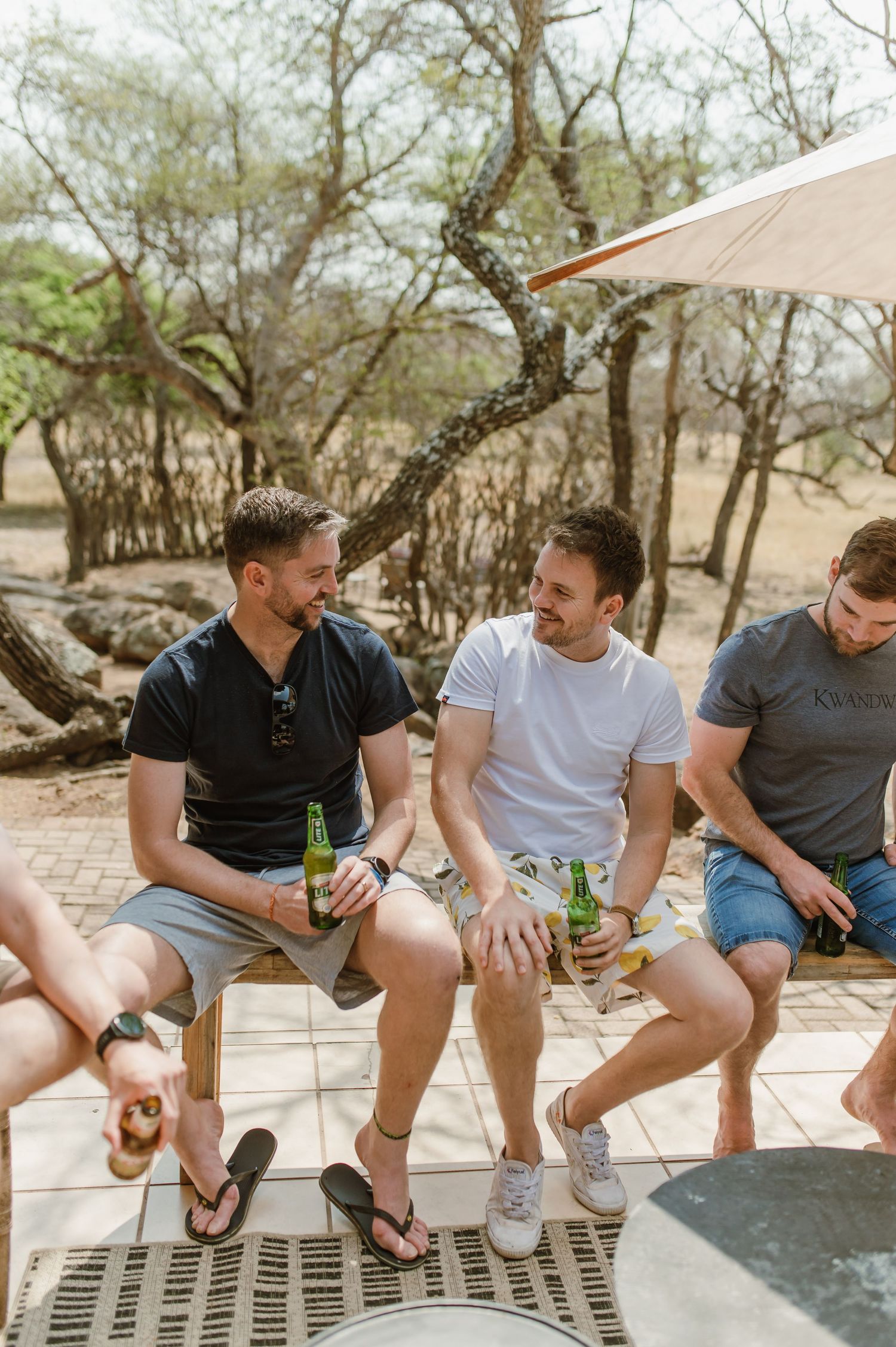 Friends sitting on a ledge having drinks and casual conversation outdoors.