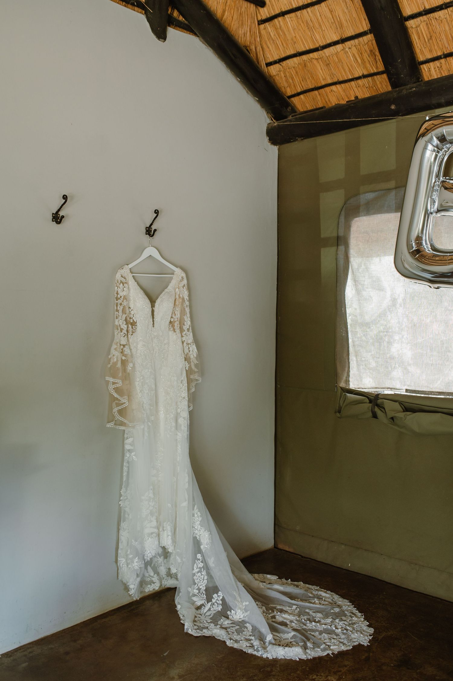 An elegant lace wedding dress with long sleeves hangs displayed against a white wall.