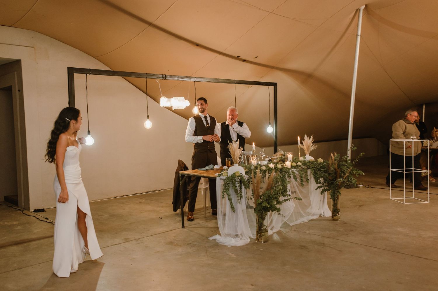 Wedding reception tent interior with string lights and elegant table settings.