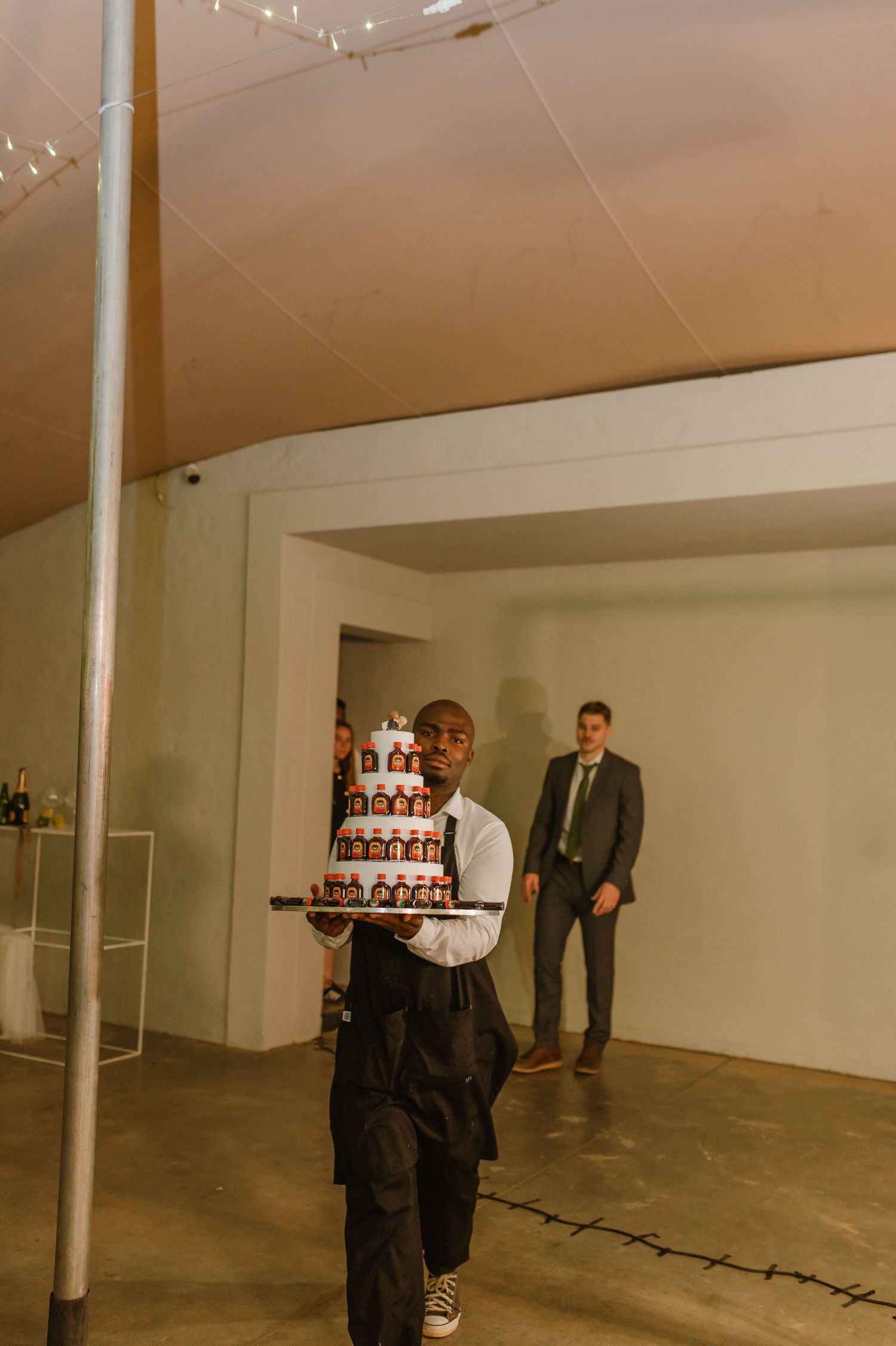 Wedding cake made of stacked Jagermeister bottles being carried by server at reception.