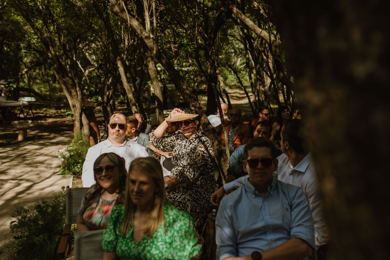 Wedding attendees seated in a shaded outdoor venue during a ceremony.